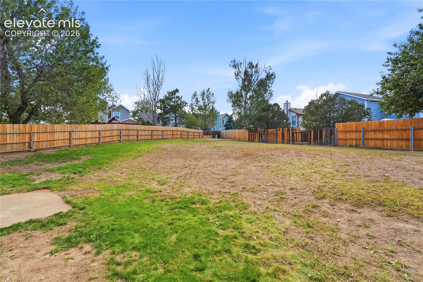 Expansive outdoor space featuring a perimeter wood fence and a concrete pad