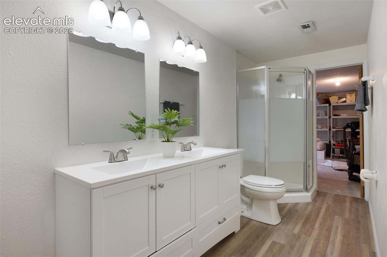 Bathroom featuring wood finished floors, a shower stall, double vanity, toilet, and a textured wall
