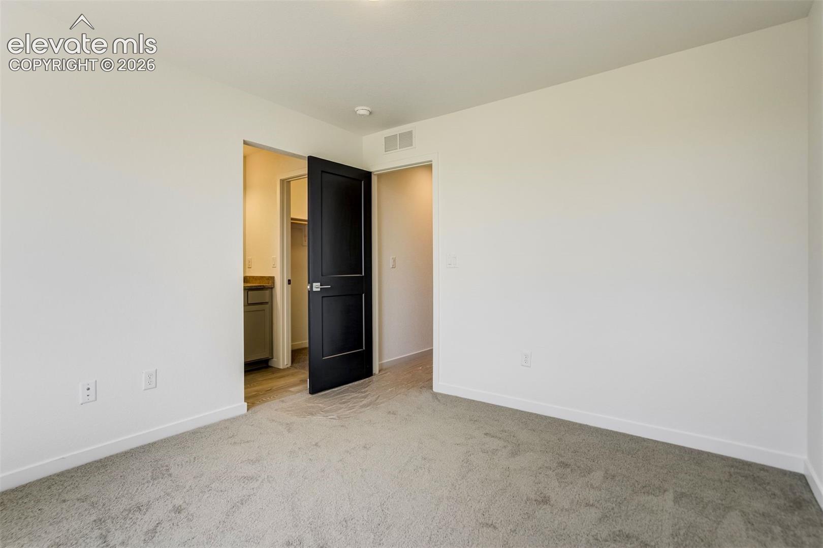 Neutral-toned wall-to-wall carpeting, high-contrast dark-finish paneled door, and neutral wall palette