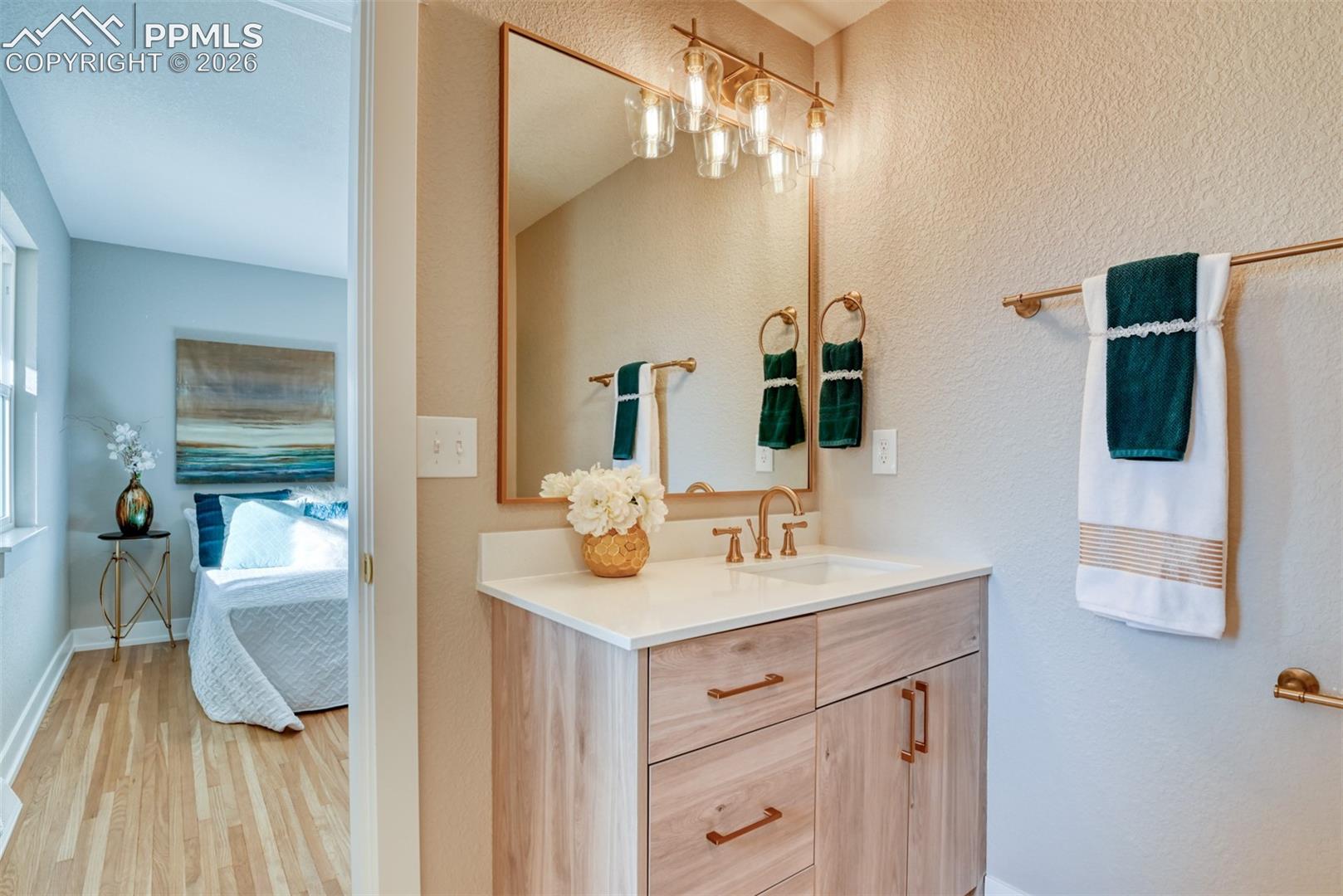 Ensuite bathroom with vanity, light wood-style floors, and a textured wall