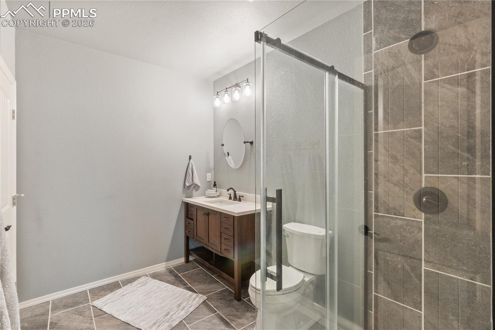 Bathroom featuring a stall shower, vanity, and dark tile patterned floors