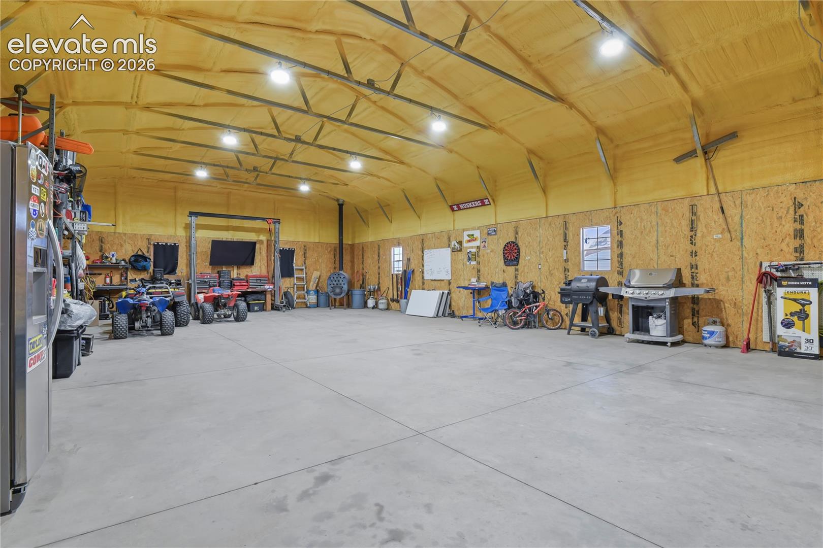 Spacious workshop featuring concrete flooring, spray-foam insulation, exposed steel trusses, and LED overhead lighting