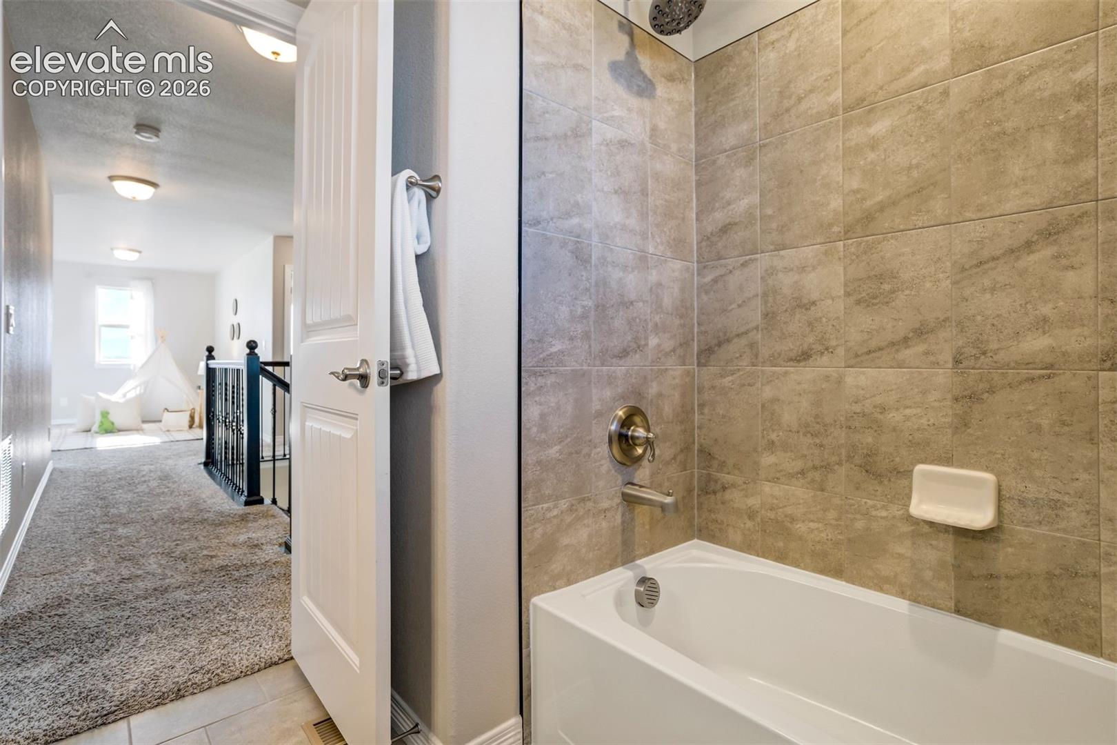 Bathtub with tiled surround, brushed nickel fixtures, and a rain shower head