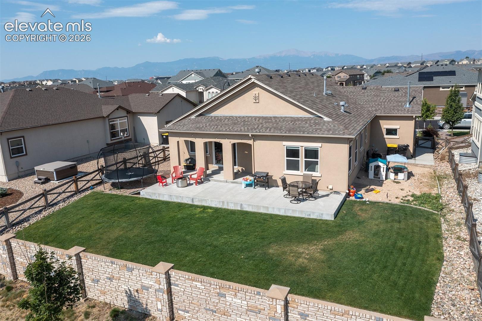 Expansive backyard featuring a concrete patio, a manicured lawn, and a stone retaining wall