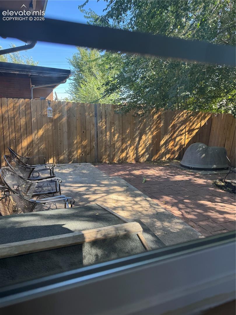 Expansive backyard retreat featuring a wood-finish fence, mature shade trees, concrete patio with defined seating areas, pergola structure overhead, and a built-in fire pit for entertaining