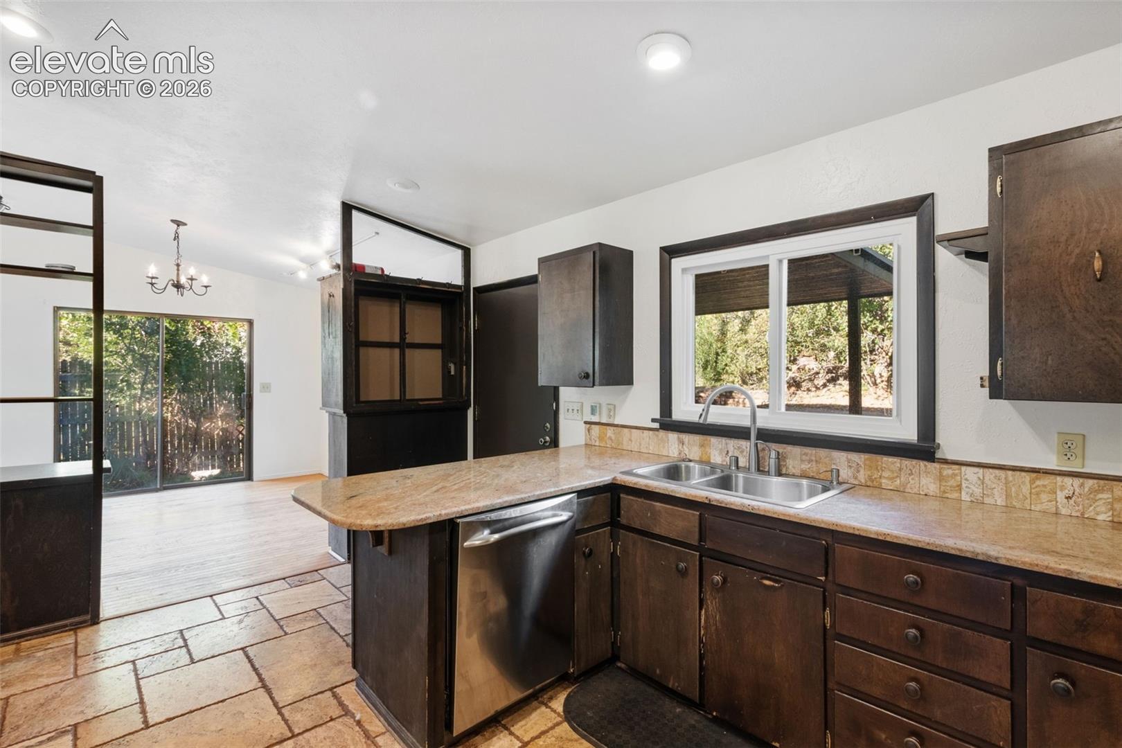 Kitchen featuring stone-finish countertops, stainless steel dishwasher, dual-basin stainless steel sink, wood-finish cabinetry, and stone tile flooring