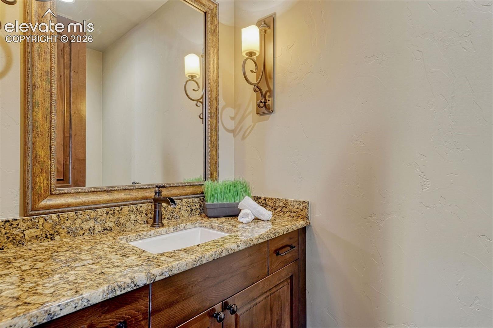 Wood-finish vanity with an undermount sink, bronze-finish faucet, and granite countertop