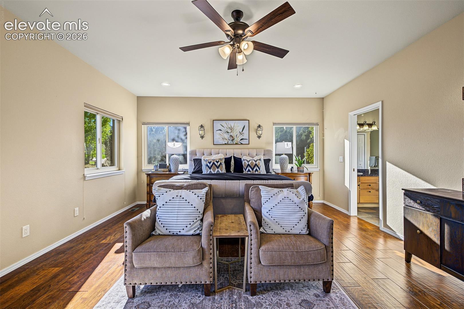 Spacious main-level primary bedroom featuring hardwood floors, a comfortable sitting area, mountain views, and sliding glass doors opening to the back balcony. Direct access to the private ensuite bathroom.