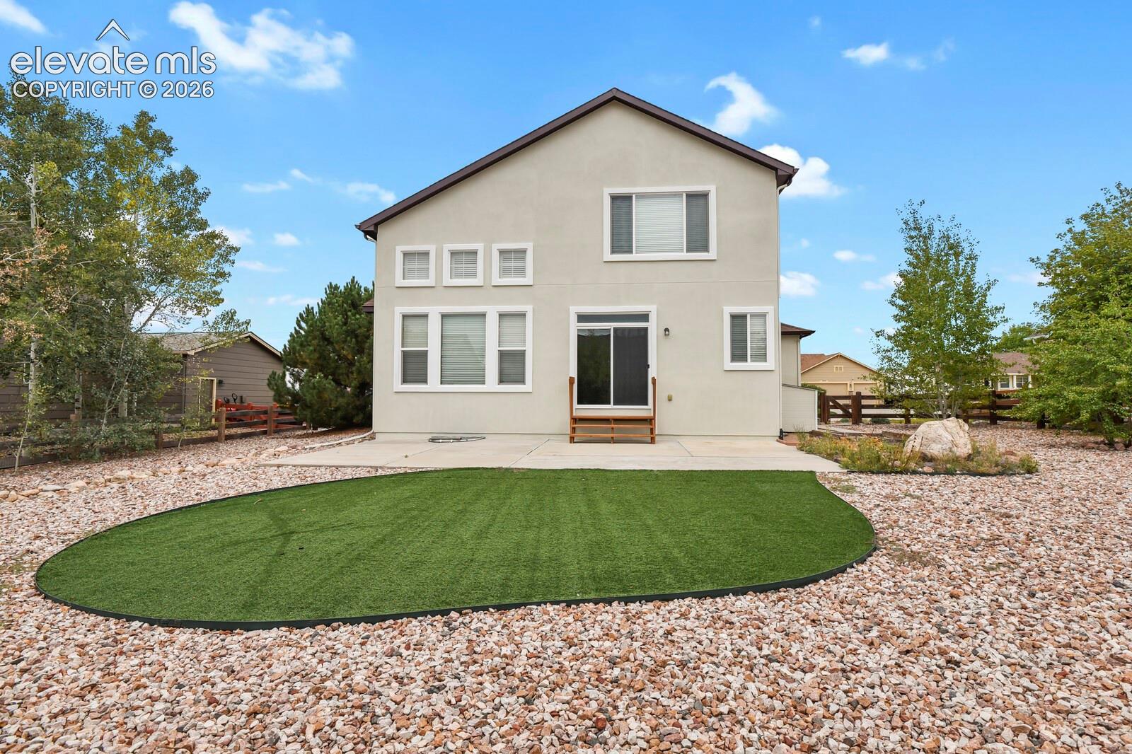 Rear elevation featuring a concrete patio, sliding glass door, and a low-maintenance artificial turf lawn