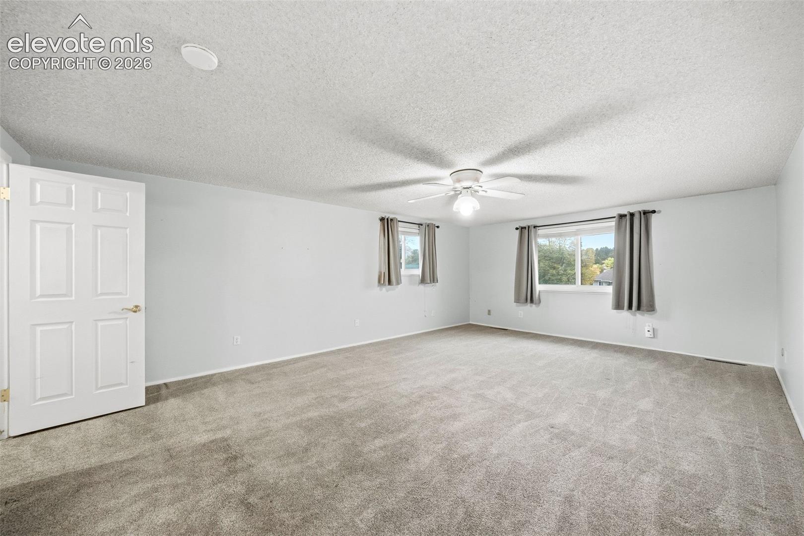 Neutral-toned carpeting, white six-panel interior door, and ceiling fan with integrated lighting