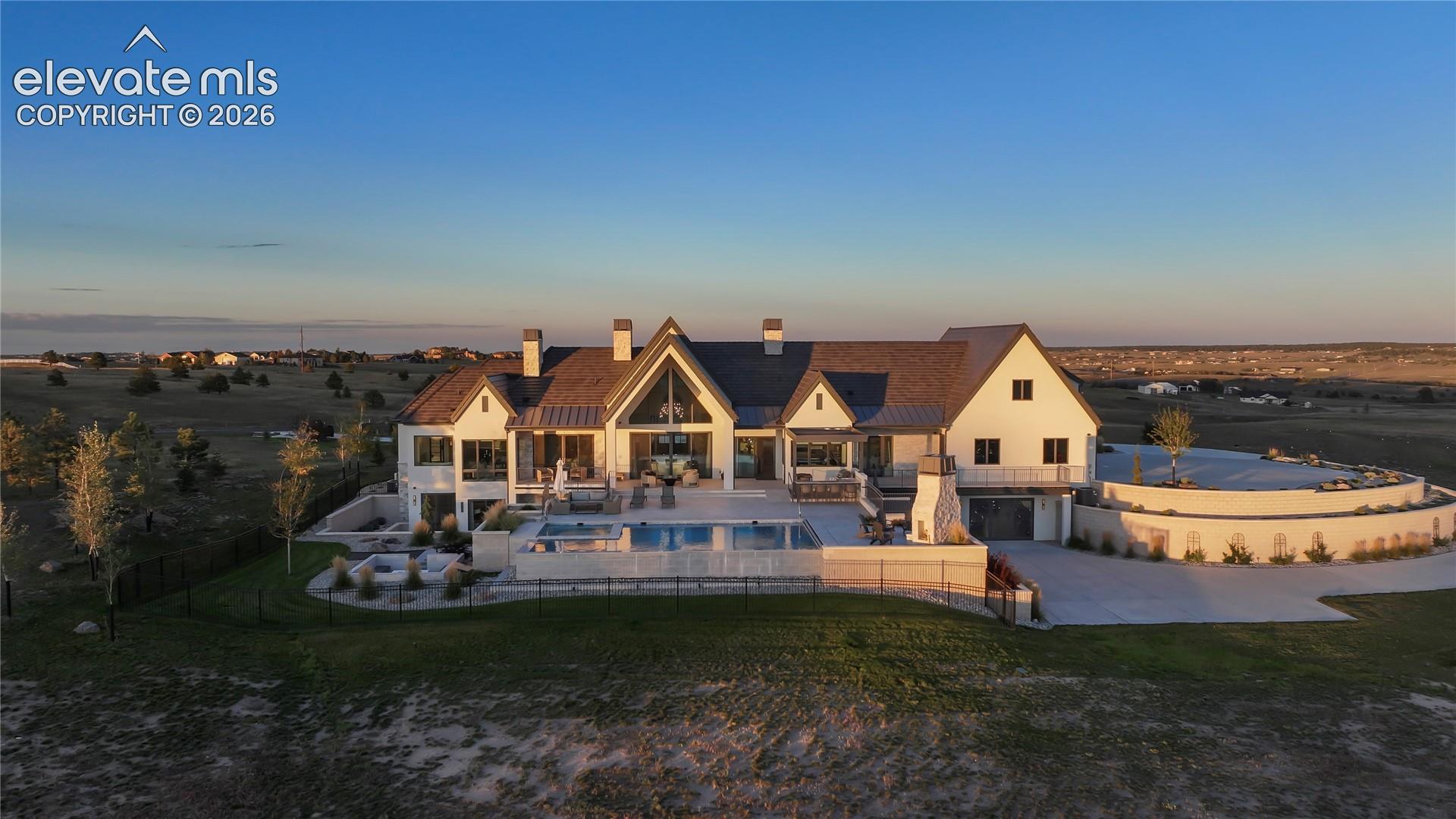 Custom estate featuring light-toned exterior siding, a multi-gabled roofline, an integrated swimming pool with spa, an outdoor stone fireplace, and a circular concrete driveway