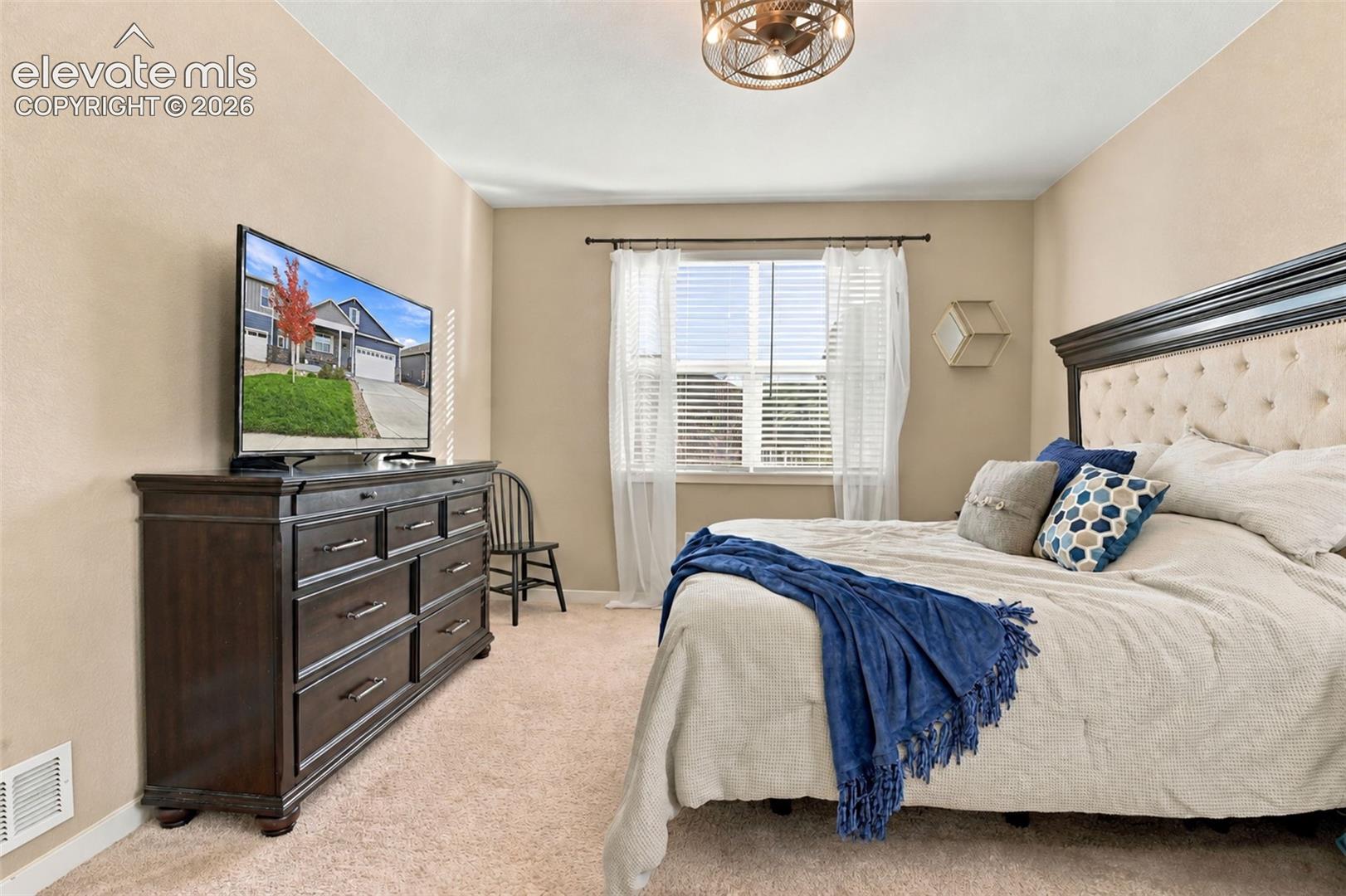 Neutral-toned carpeted interior featuring a single-window configuration with horizontal blinds and a decorative metal-finish ceiling fan with exposed bulb lighting