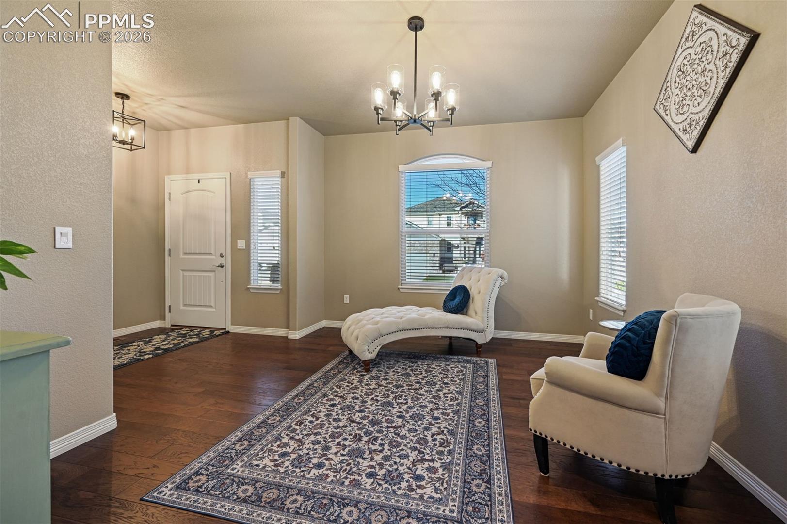 Sitting room featuring dark wood-style flooring, a chandelier, and a textured wall