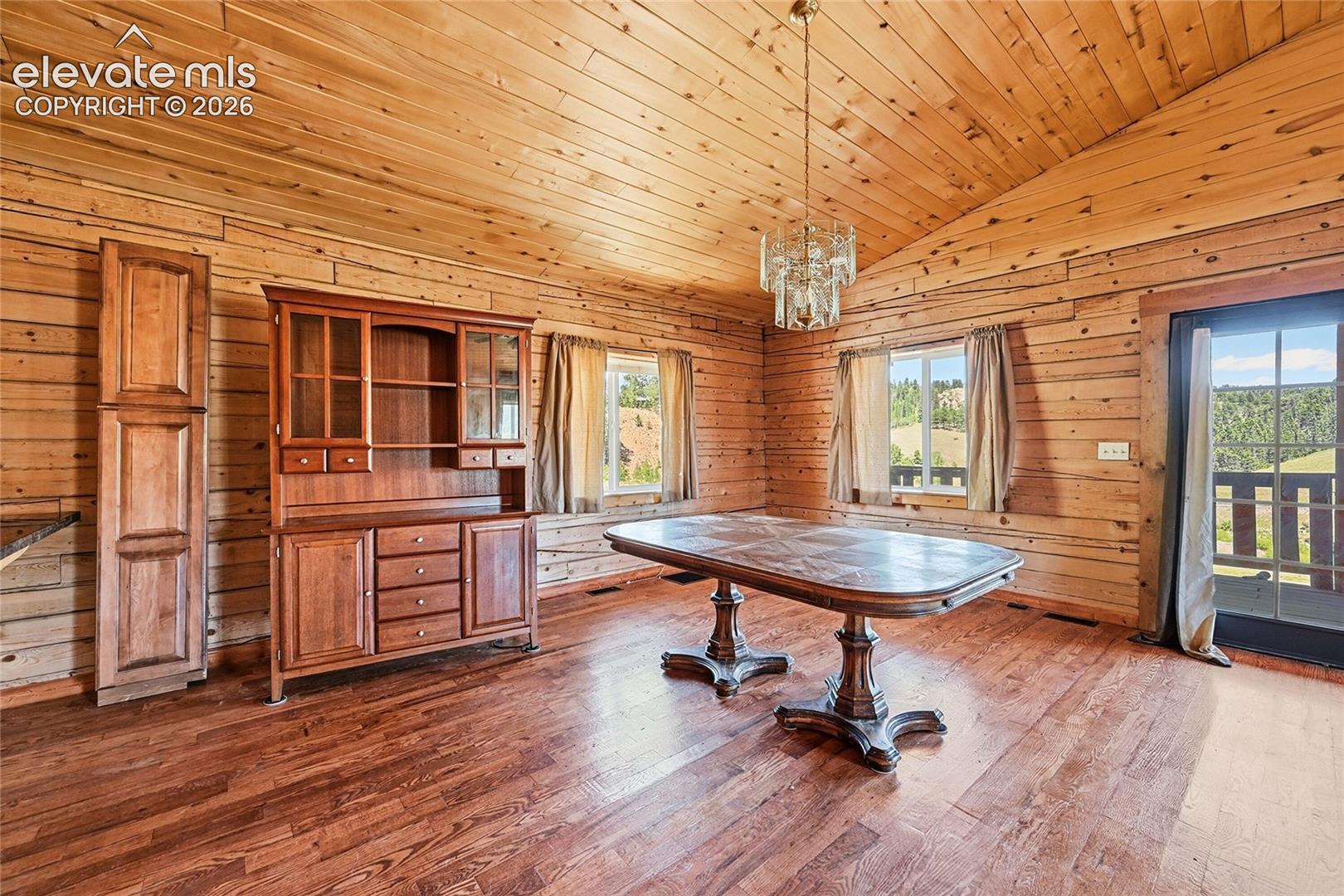 Sloped wood-paneled ceiling with a chandelier, wood-finish walls, and wood-finish flooring