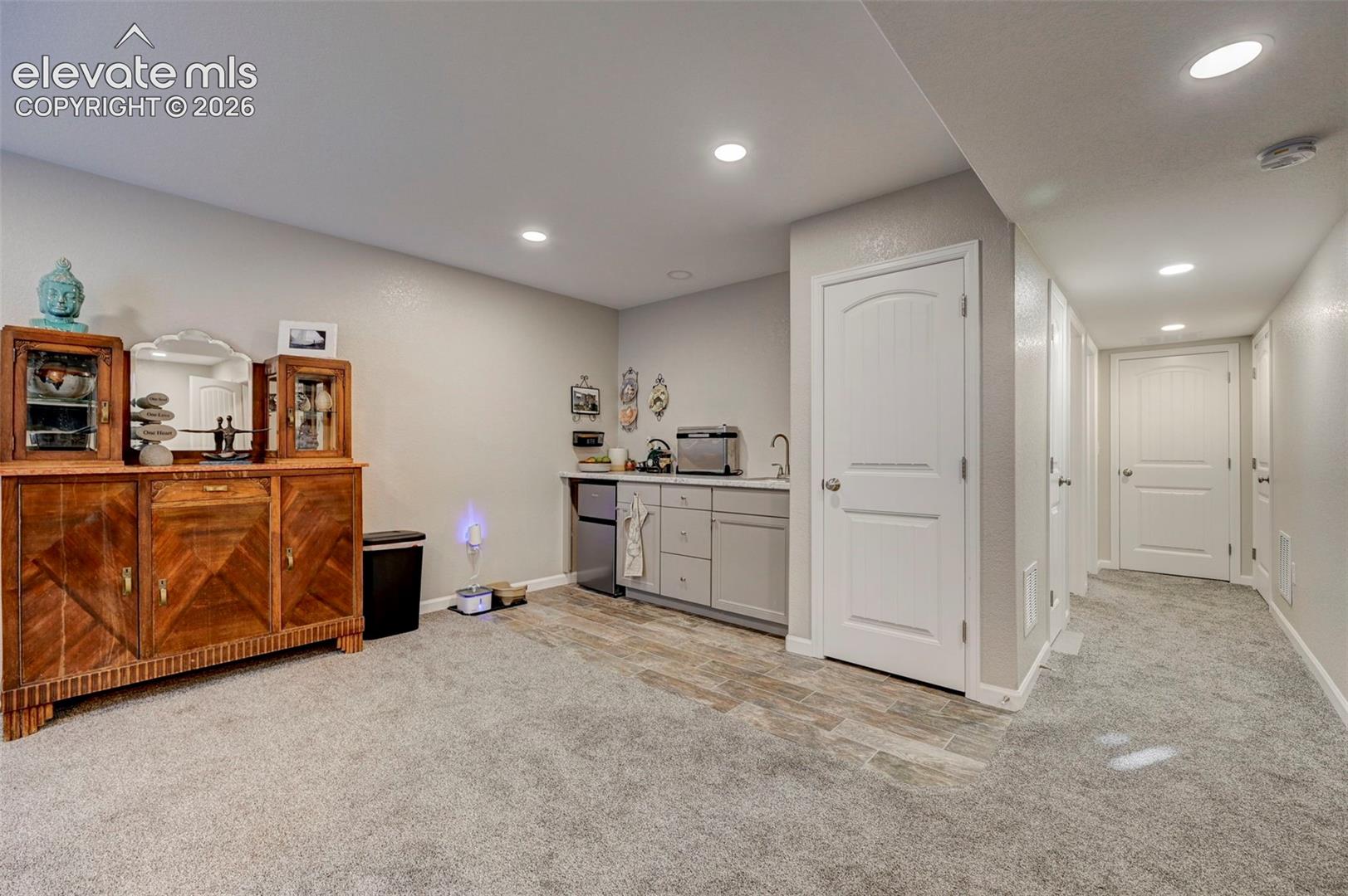Wet bar featuring cabinetry, a sink, and stone-tile flooring, complemented by recessed lighting and neutral wall-to-wall carpeting