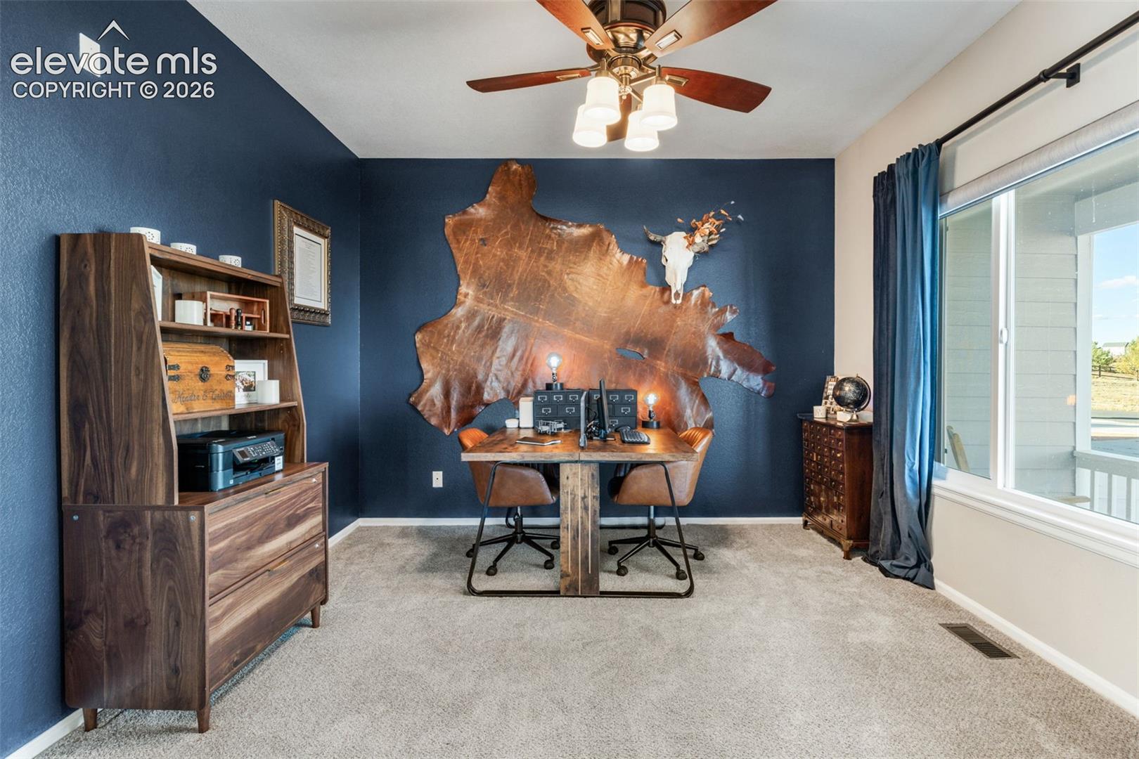 Room featuring deep-toned accent walls, neutral carpeting, and a ceiling fan with integrated lighting