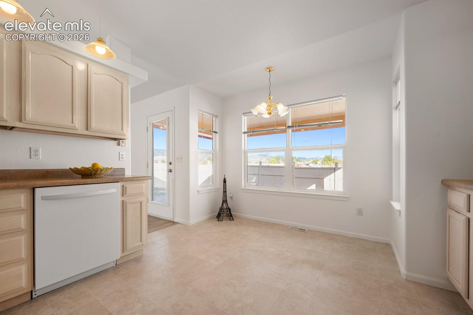 Kitchen featuring shaker-style cabinetry, white appliance suite, tile flooring, multi-pane windows, and a multi-light pendant chandelier