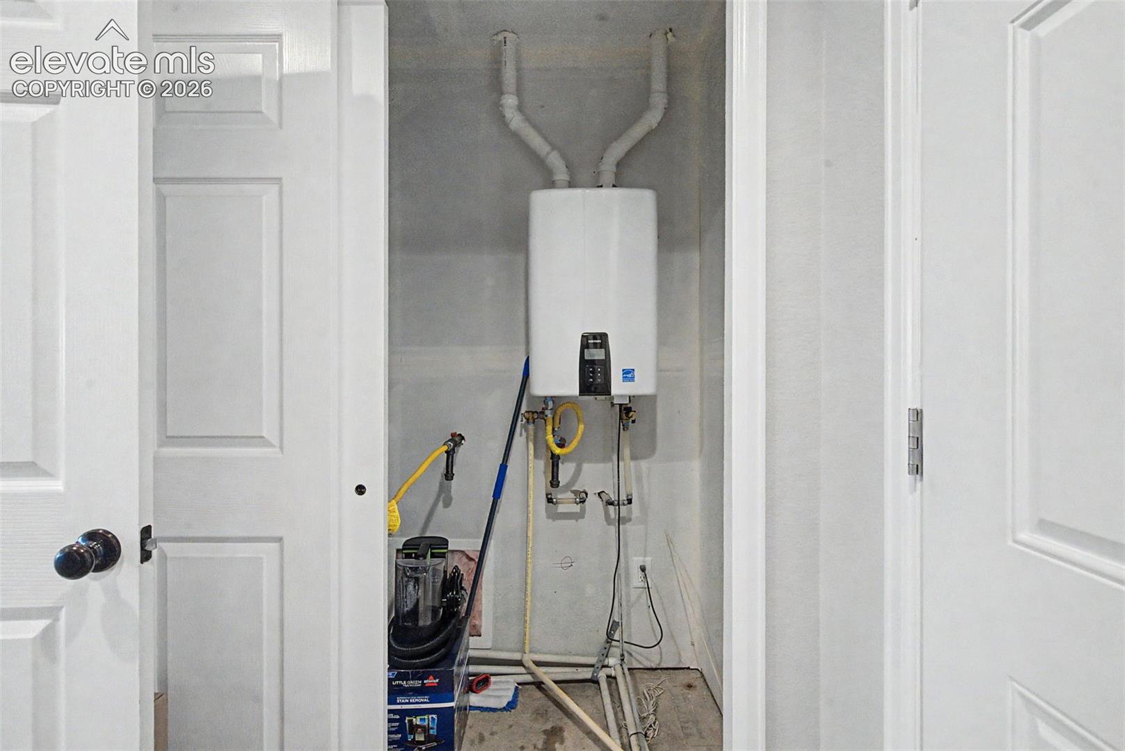 Built-in mechanical closet featuring a wall-mounted tankless water heater, exposed utility piping, and a concrete floor