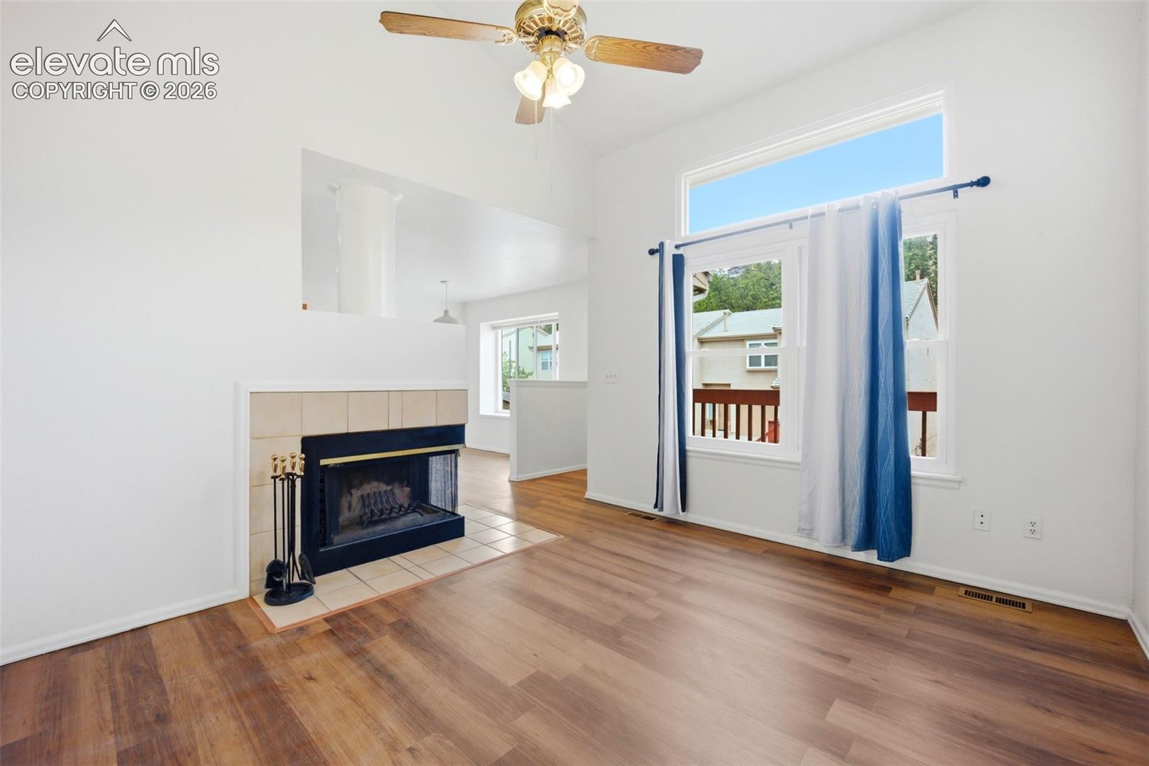 Vaulted ceiling living area featuring wood-finish flooring, a wood-burning fireplace with a tile surround, and a clerestory window