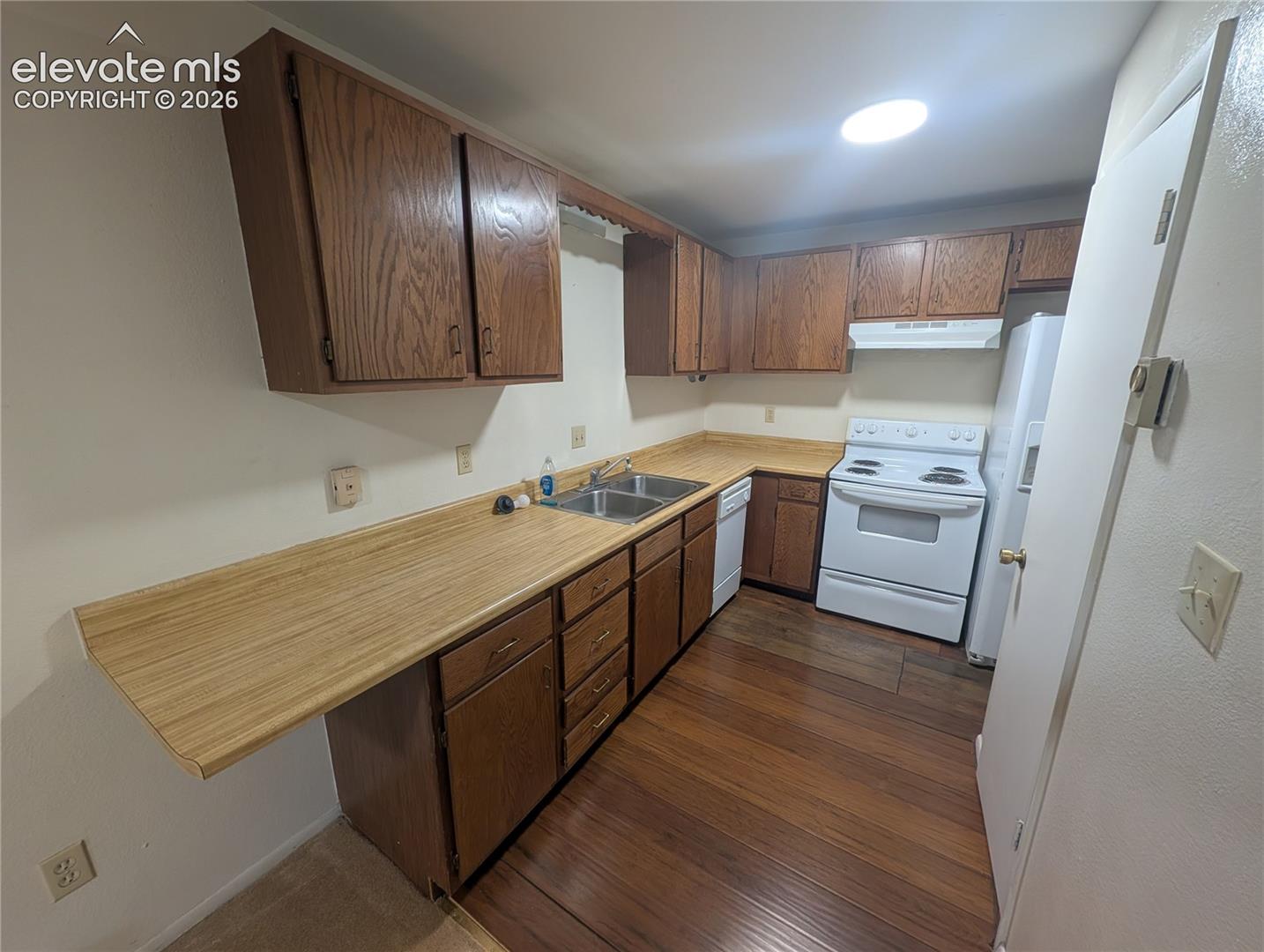 Kitchen featuring wood-finish flooring, wood cabinetry, white appliances, and a double basin sink