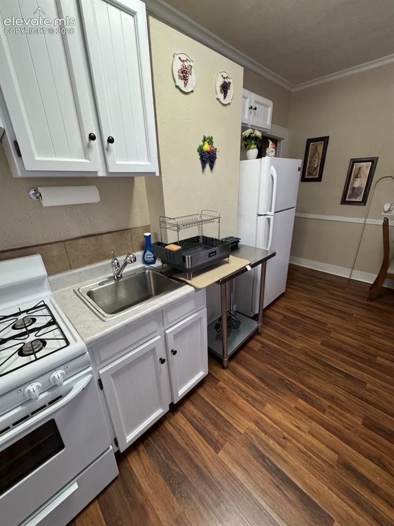 White cabinetry with dark hardware, stainless steel sink, white freestanding range, white refrigerator, and wood-finish flooring