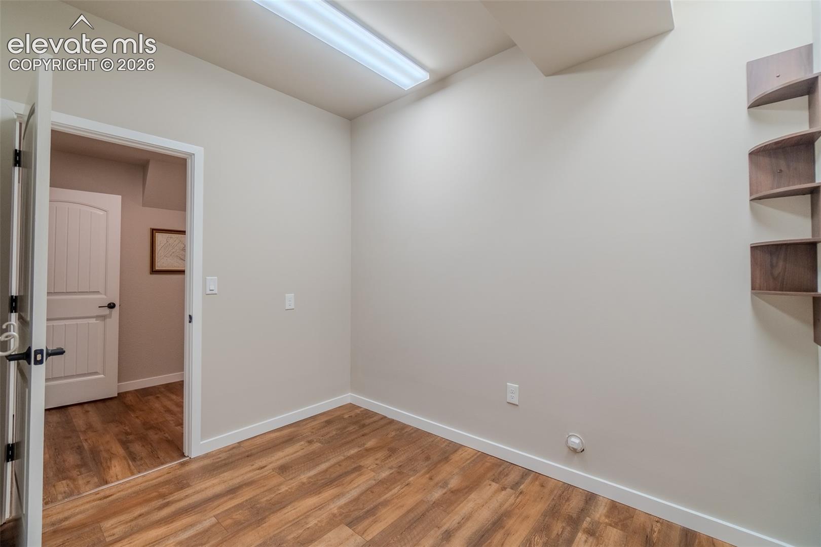 Room featuring wood-finish flooring, light-toned walls, white trim, and a built-in wall shelf unit