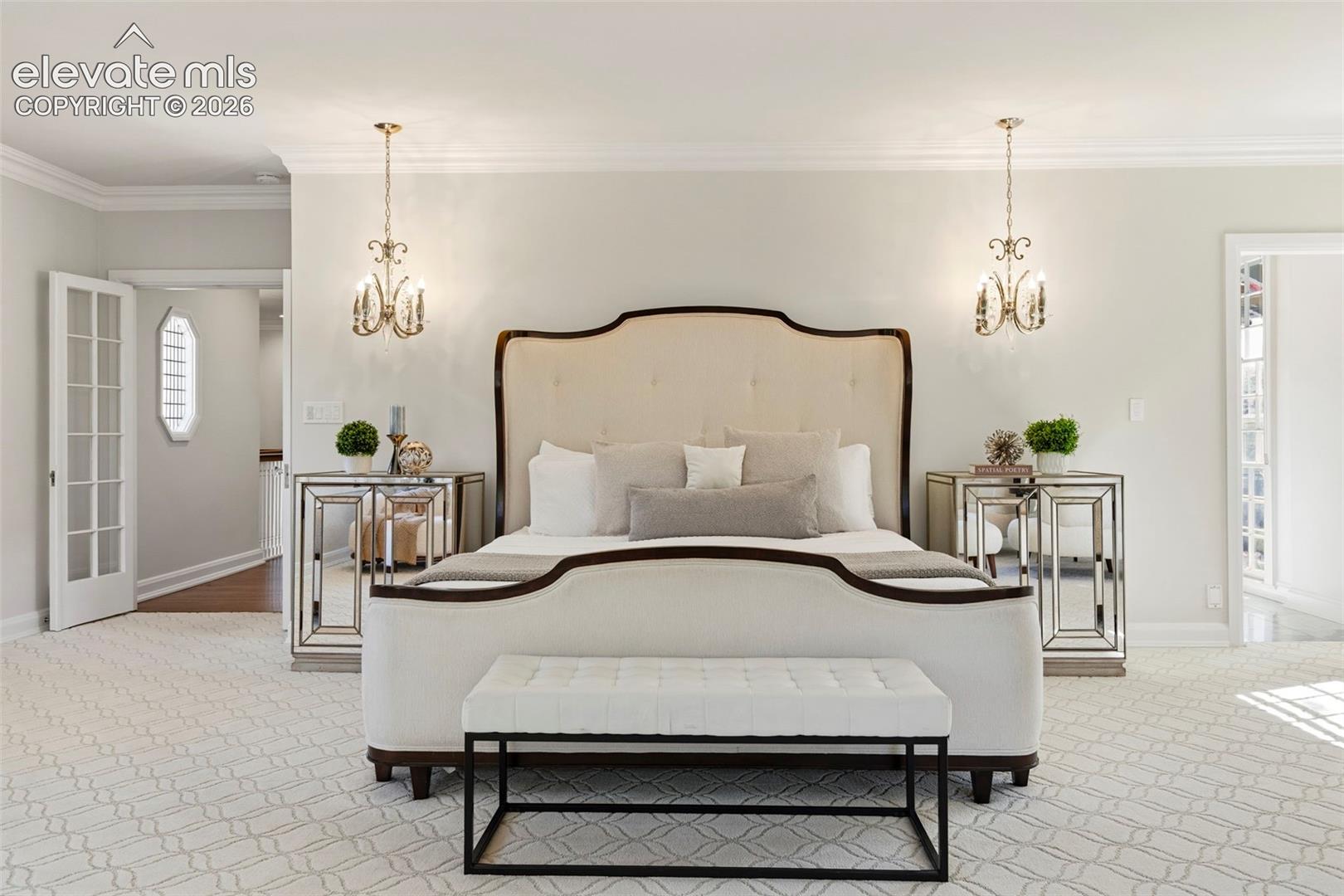 Patterned carpet flooring, dual ceiling-mounted chandeliers, crown molding, and French-style interior doors