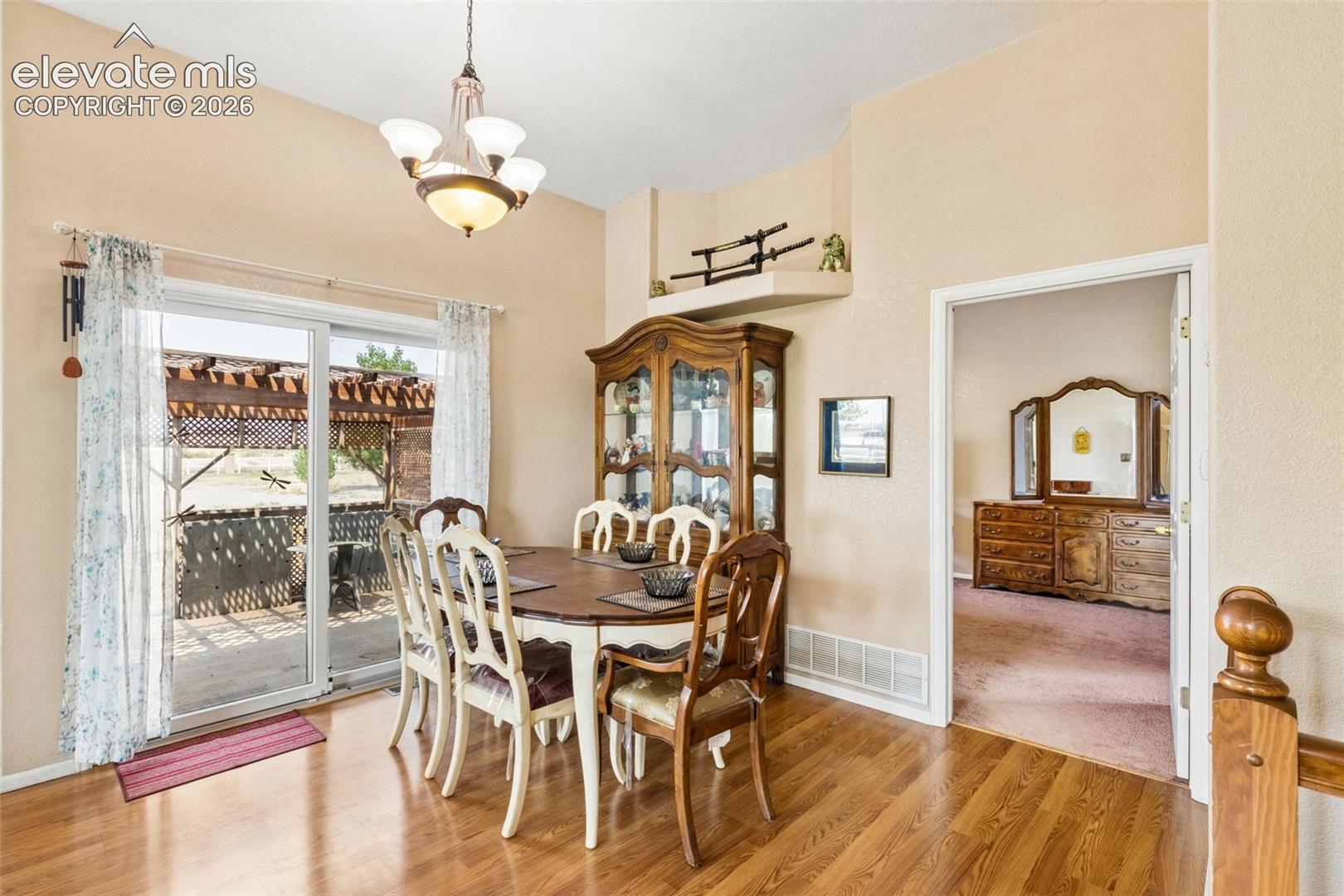 Dining area featuring wood-finish flooring, a vaulted ceiling with a multi-light chandelier, a built-in recessed display niche, and a sliding glass door providing external access