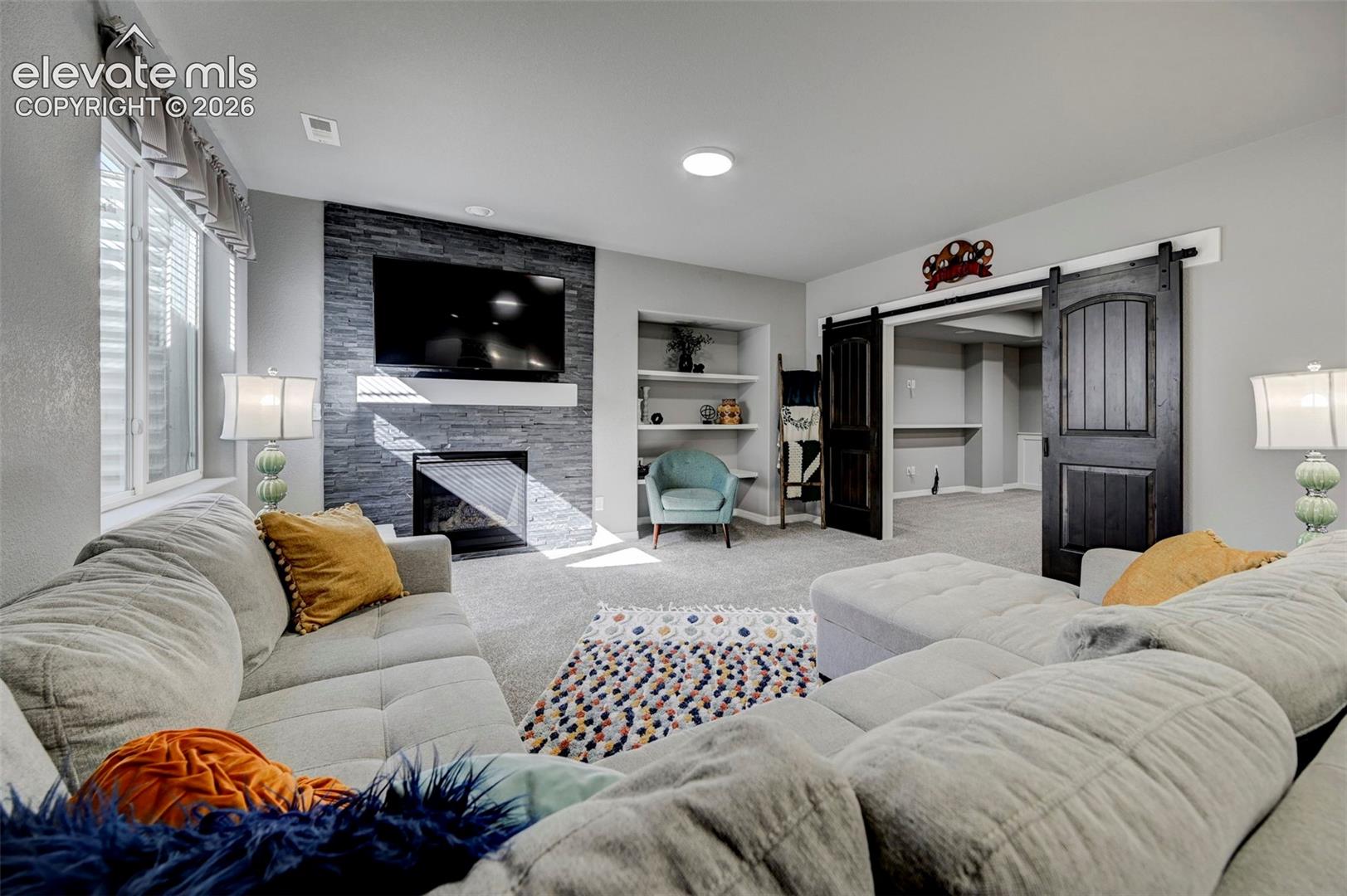 Spacious living area featuring a stacked stone fireplace with a floating mantel, recessed lighting, and large windows