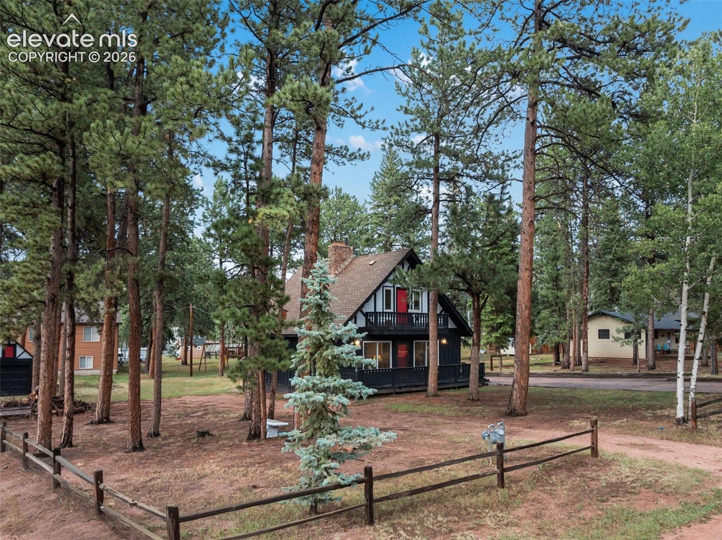 A-frame property with a second-story balcony, prominent red front door, and a split-rail fence