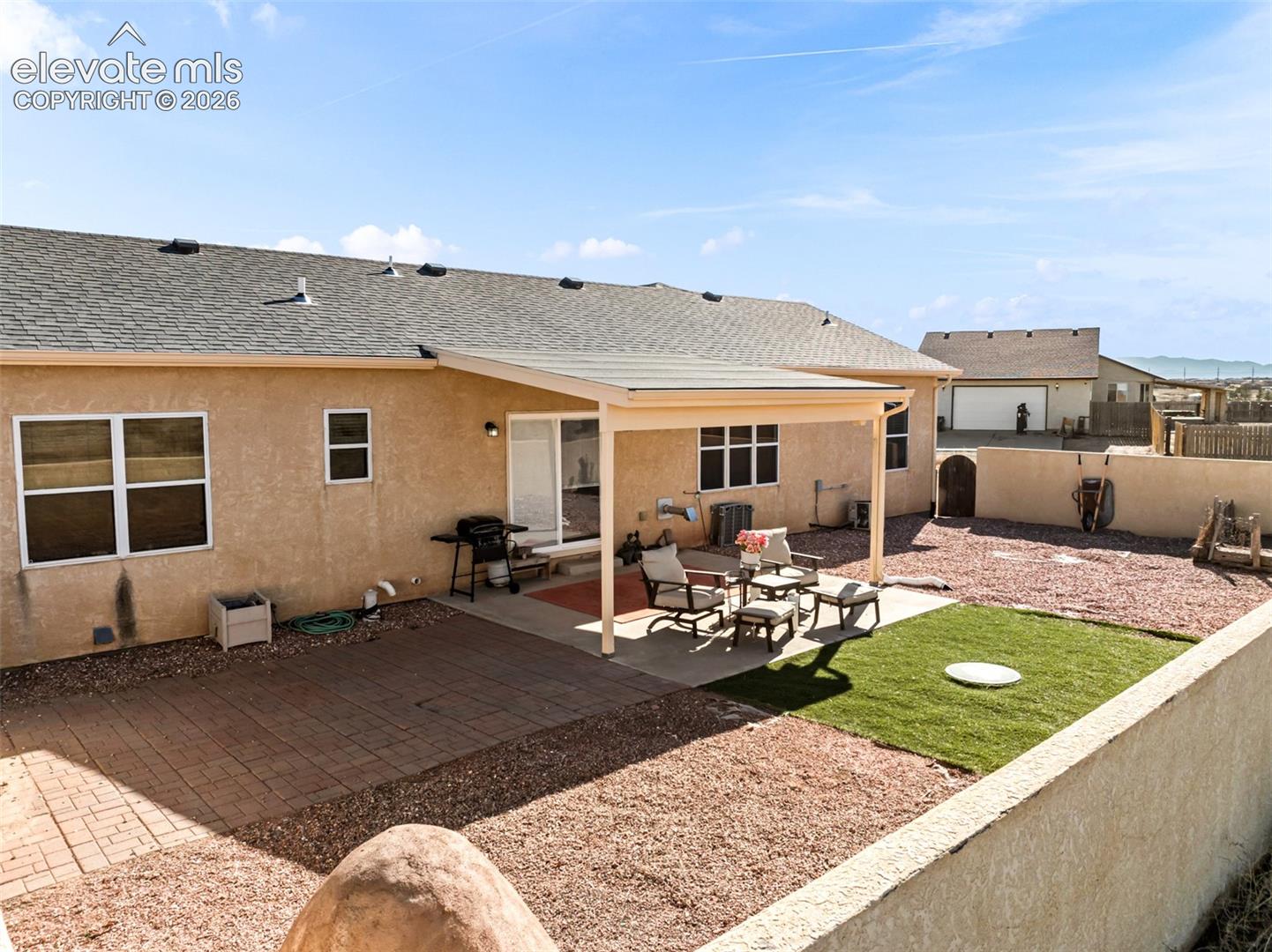 Expansive backyard featuring a covered patio, artificial turf area, and a paved patio space