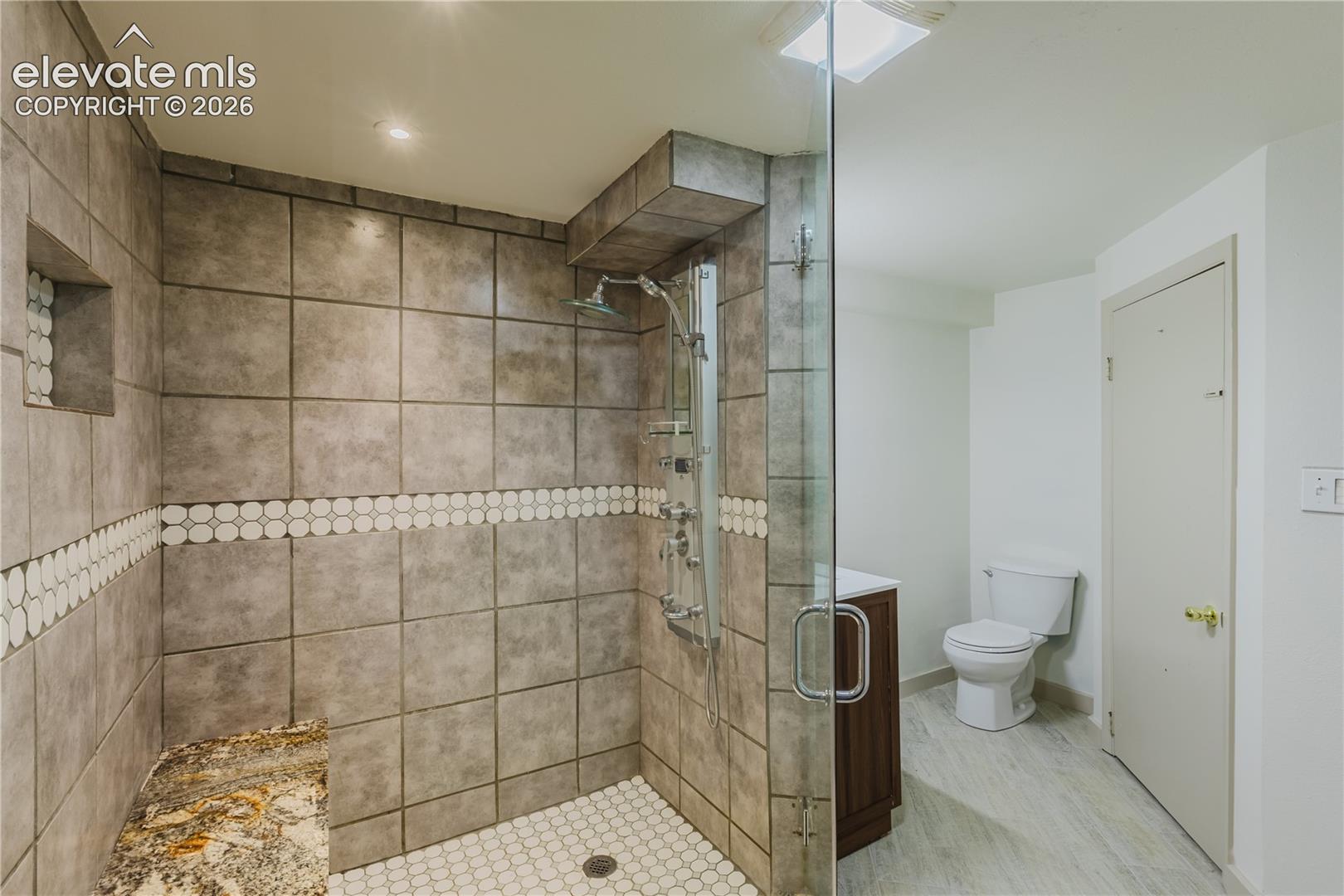 Basement 3/4 Bathroom - Enclosed shower featuring a clear glass door, large format wall tiles with a decorative mosaic band, integrated shelving, and a multi-function shower system