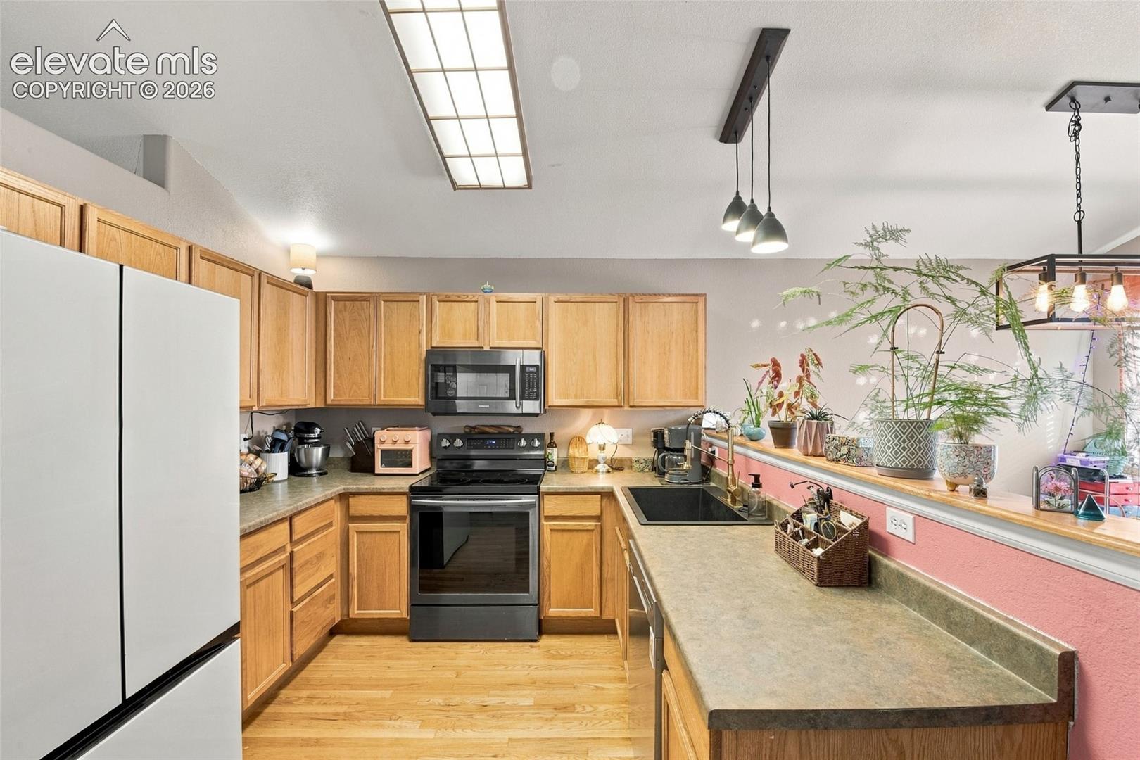 Kitchen featuring light wood cabinetry, matte finish countertops, a black undermount sink with a gooseneck faucet, integrated black appliances, and varied overhead pendant and recessed lighting