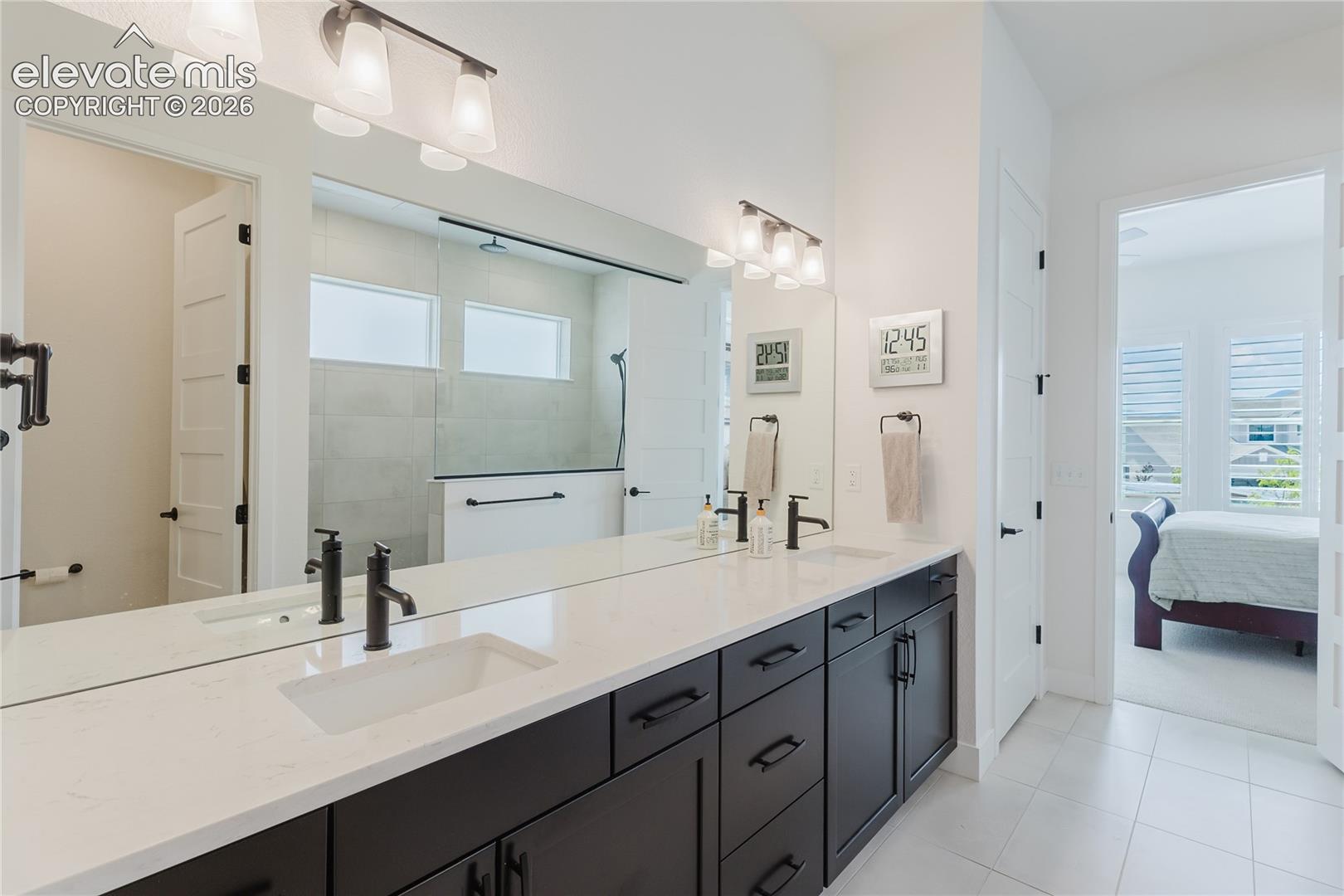 Dual vanity with integrated sinks, quartz countertop, dark wood-finish cabinetry, and a large mirror