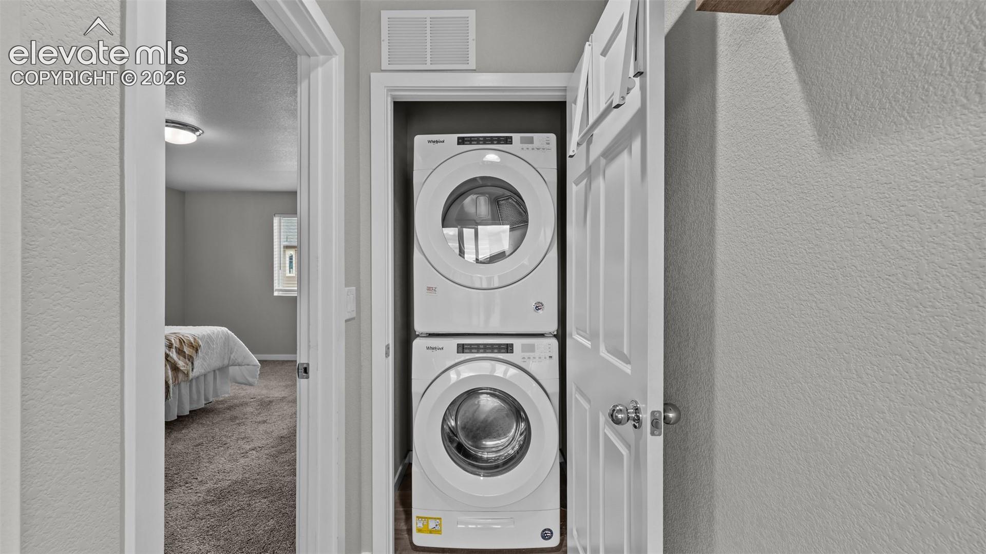 Laundry closet featuring stacked front-load washer and dryer units and a six-panel door