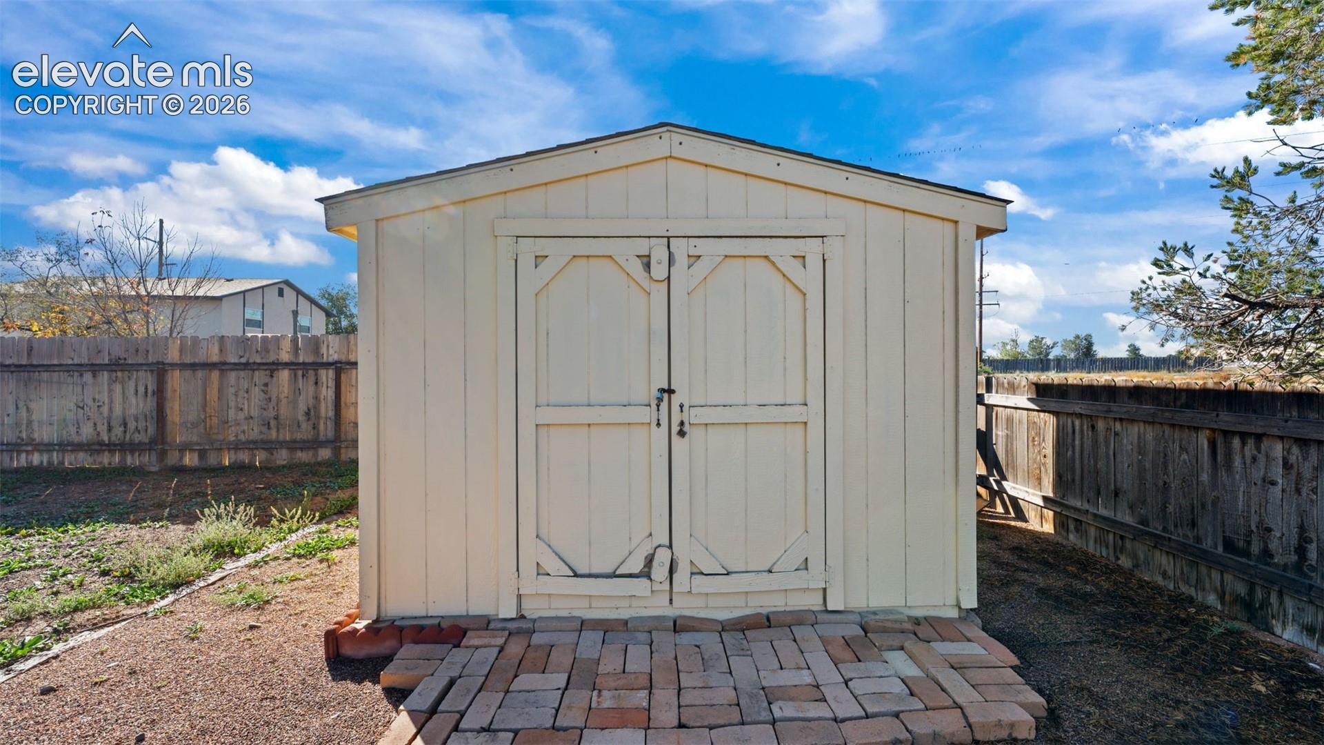 Exterior storage shed featuring a gabled roof, vertical siding, and double doors, situated on a brick paver foundation
