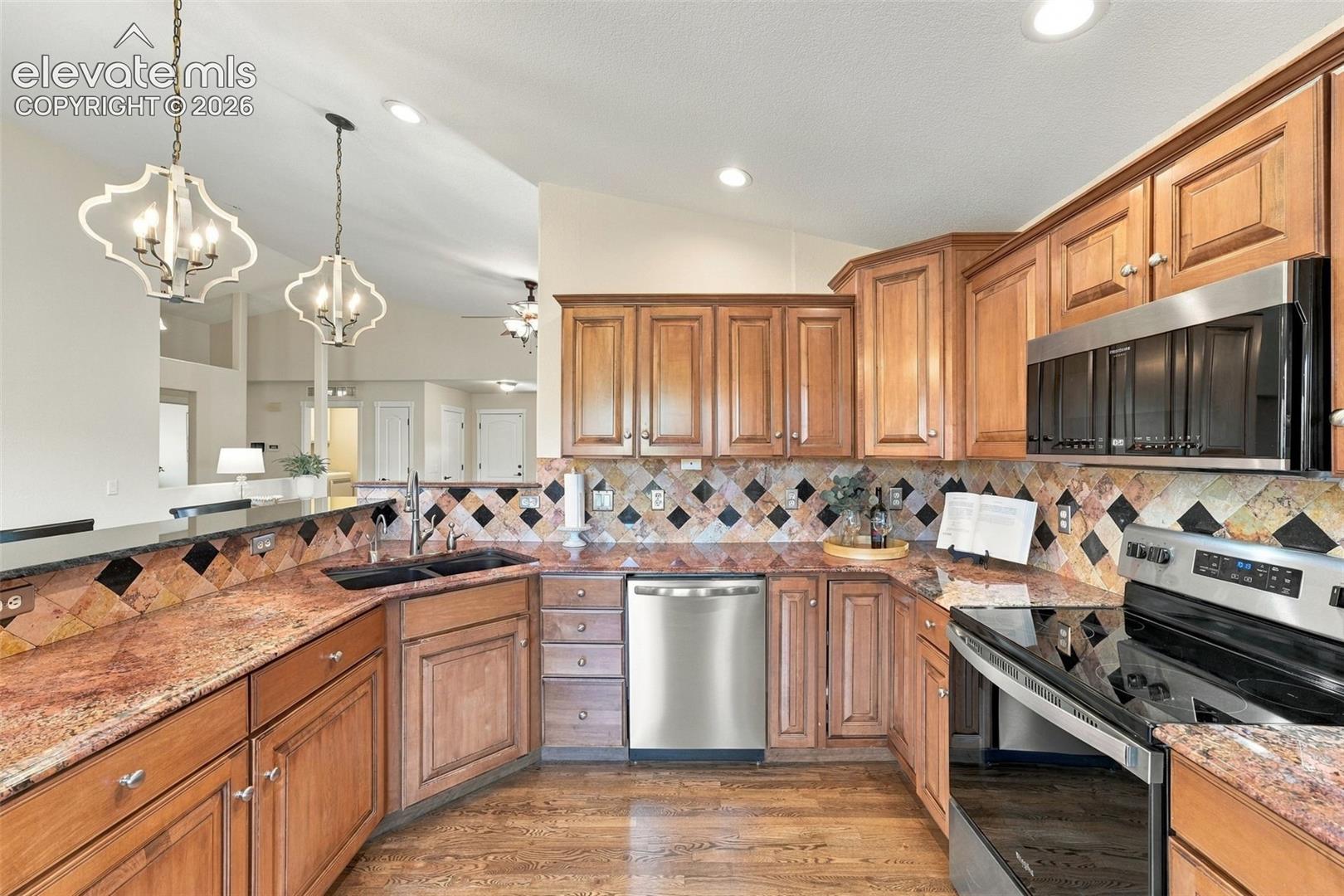 Kitchen featuring wood cabinetry, stone countertops, diamond-pattern tile backsplash, stainless steel appliances, and dual pendant lighting