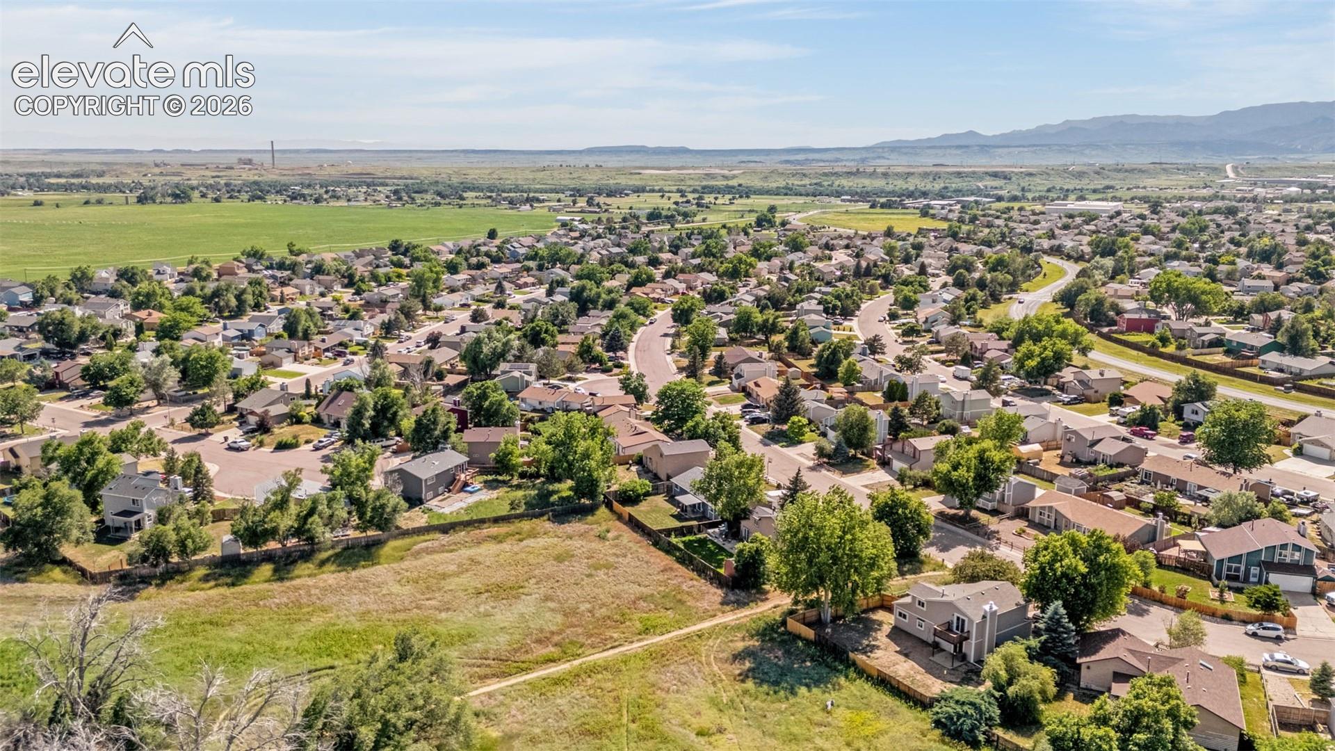 Aerial perspective of a suburban neighborhood featuring mature trees, expansive open green spaces, and mountain terrain in the distance