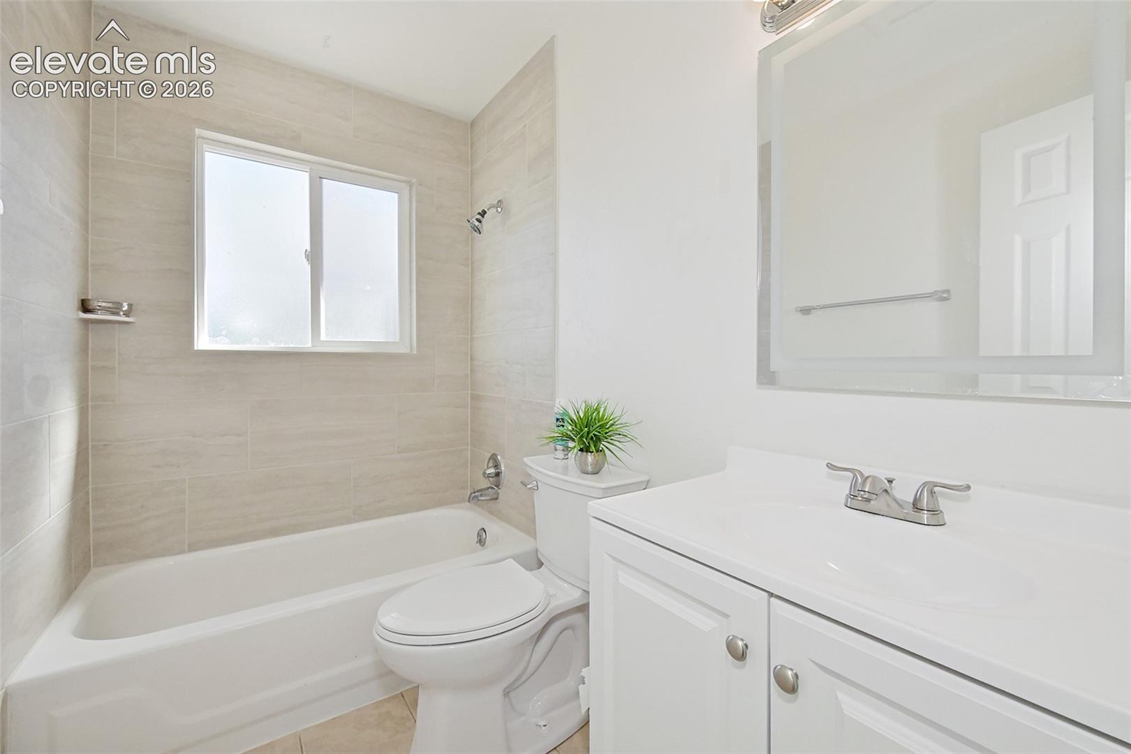Bathroom featuring a new white vanity with a solid-surface countertop, an integrated sink, a LED rectangular mirror, and shower with light-toned horizontal wall tile