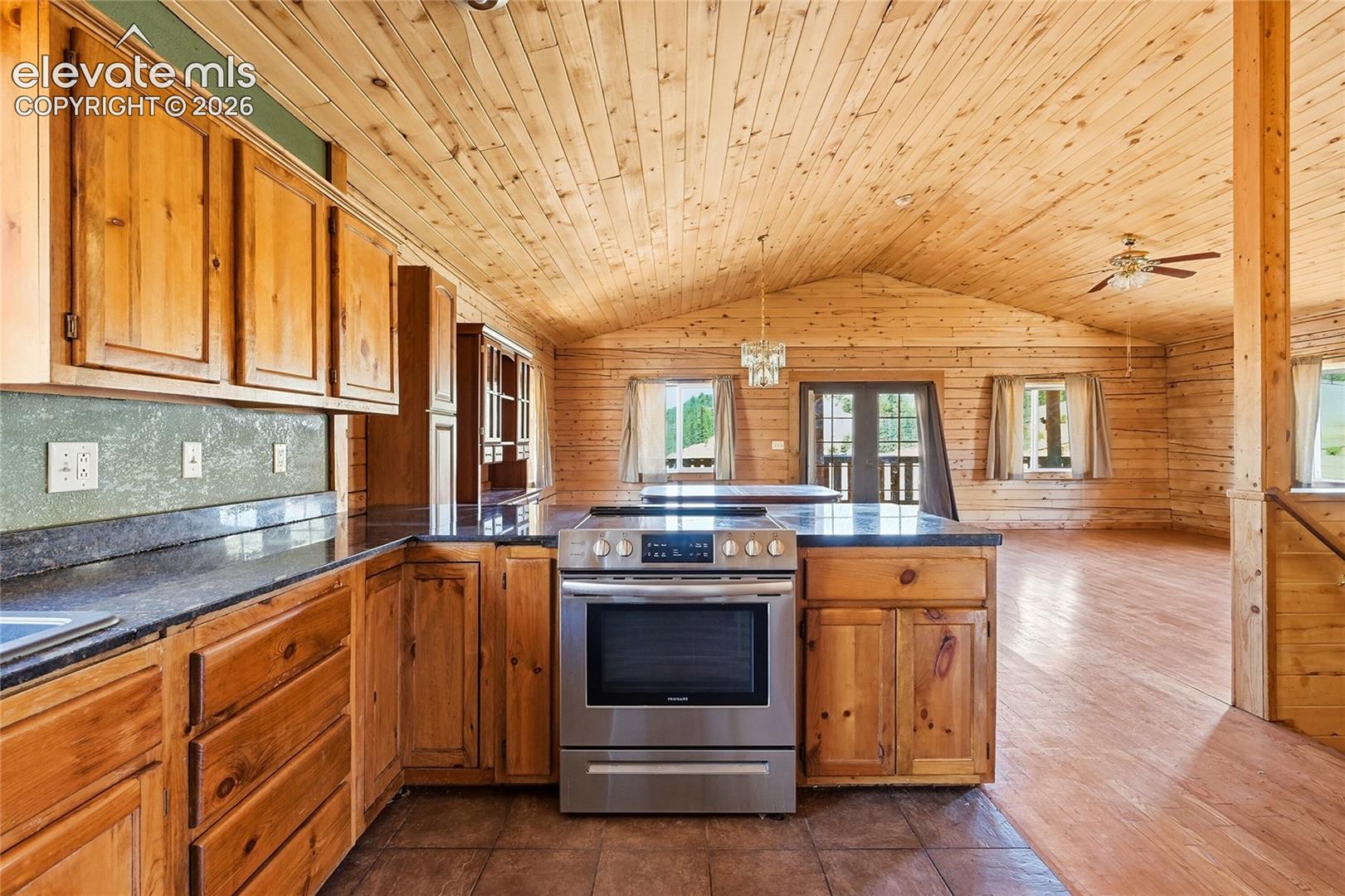 Vaulted wood-paneled ceiling, wood cabinetry, dark countertops, stainless steel range, and tile flooring