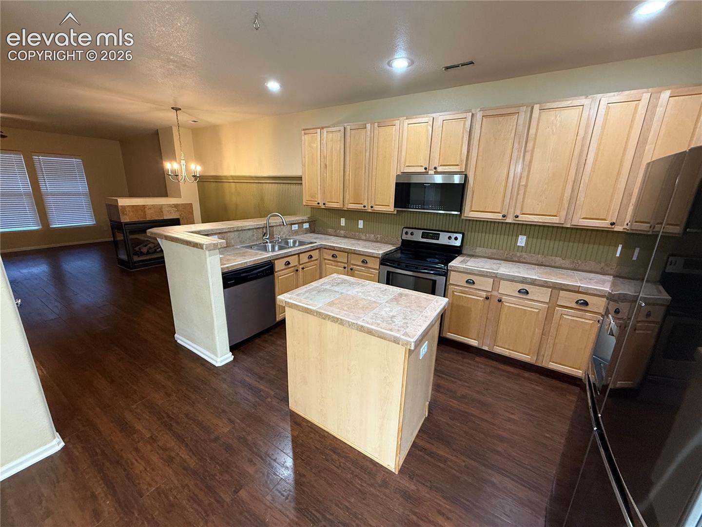 Kitchen featuring wood-finish cabinetry, a central island with tiled countertop, stainless steel appliances, and wood-finish flooring