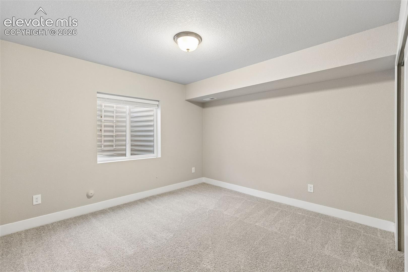Interior room featuring neutral wall paint, carpeted flooring, a recessed window with an egress well, and a flush-mount ceiling light fixture