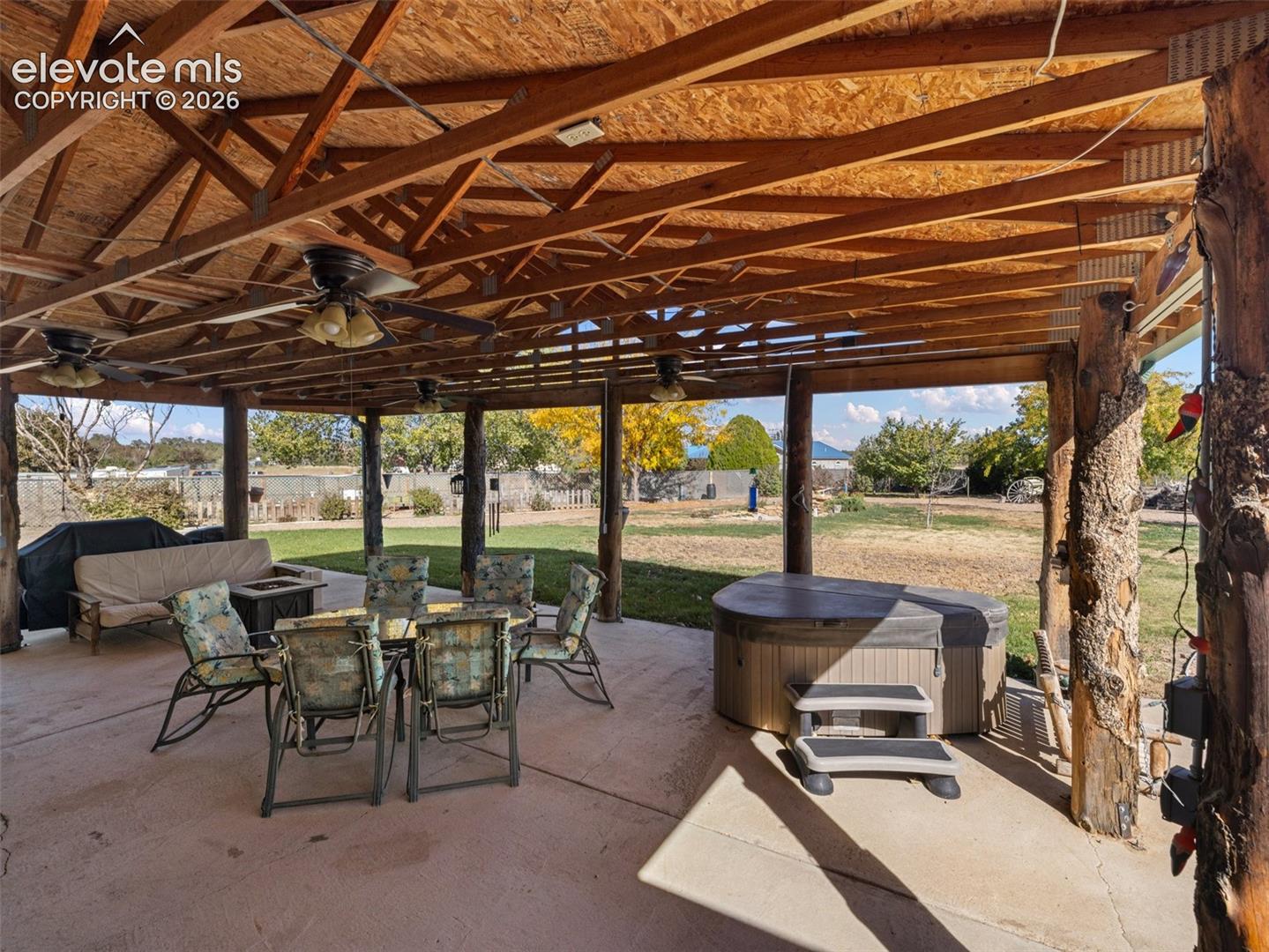Covered patio featuring an exposed timber-frame ceiling, rustic log support posts, a concrete floor, and an integrated spa