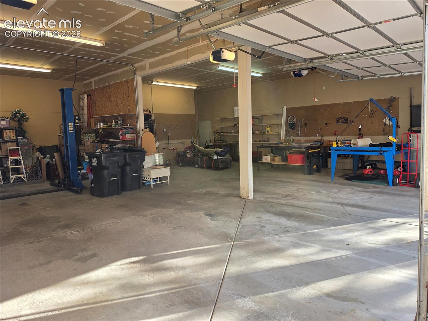 Large garage space with a concrete floor, overhead lighting, and exposed ceiling joists