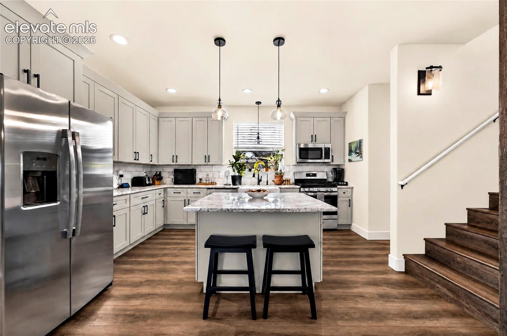 Kitchen featuring shaker-style cabinetry, a central island with stone-finish countertops, stainless steel appliances, wood-finish flooring, and recessed lighting