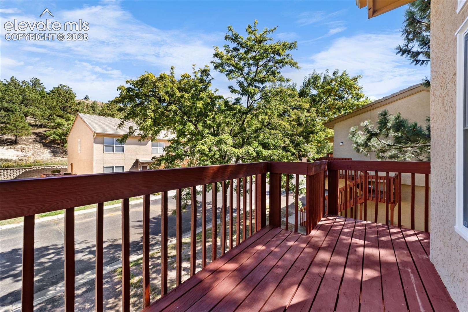 Elevated wooden deck featuring vertical slat railings and a textured stucco exterior wall