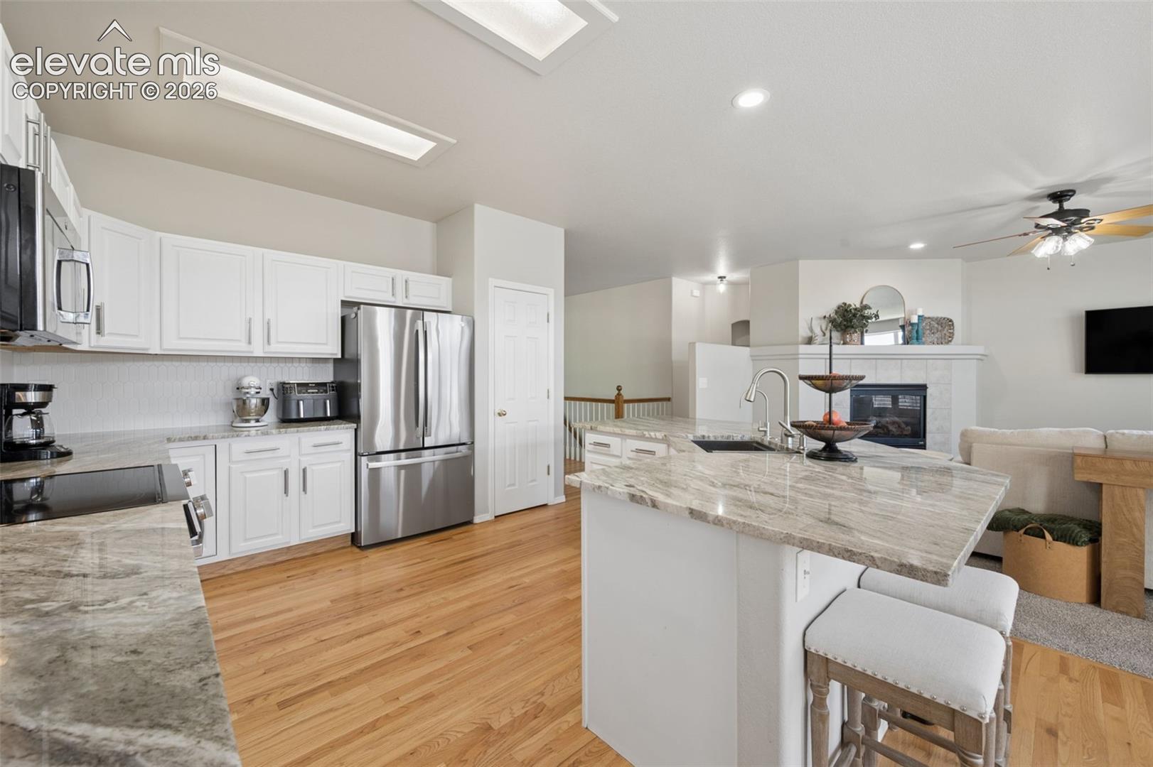 Kitchen featuring white shaker-style cabinetry, stainless steel appliances, stone-surface countertops, a center island with sink, and wood-finish flooring