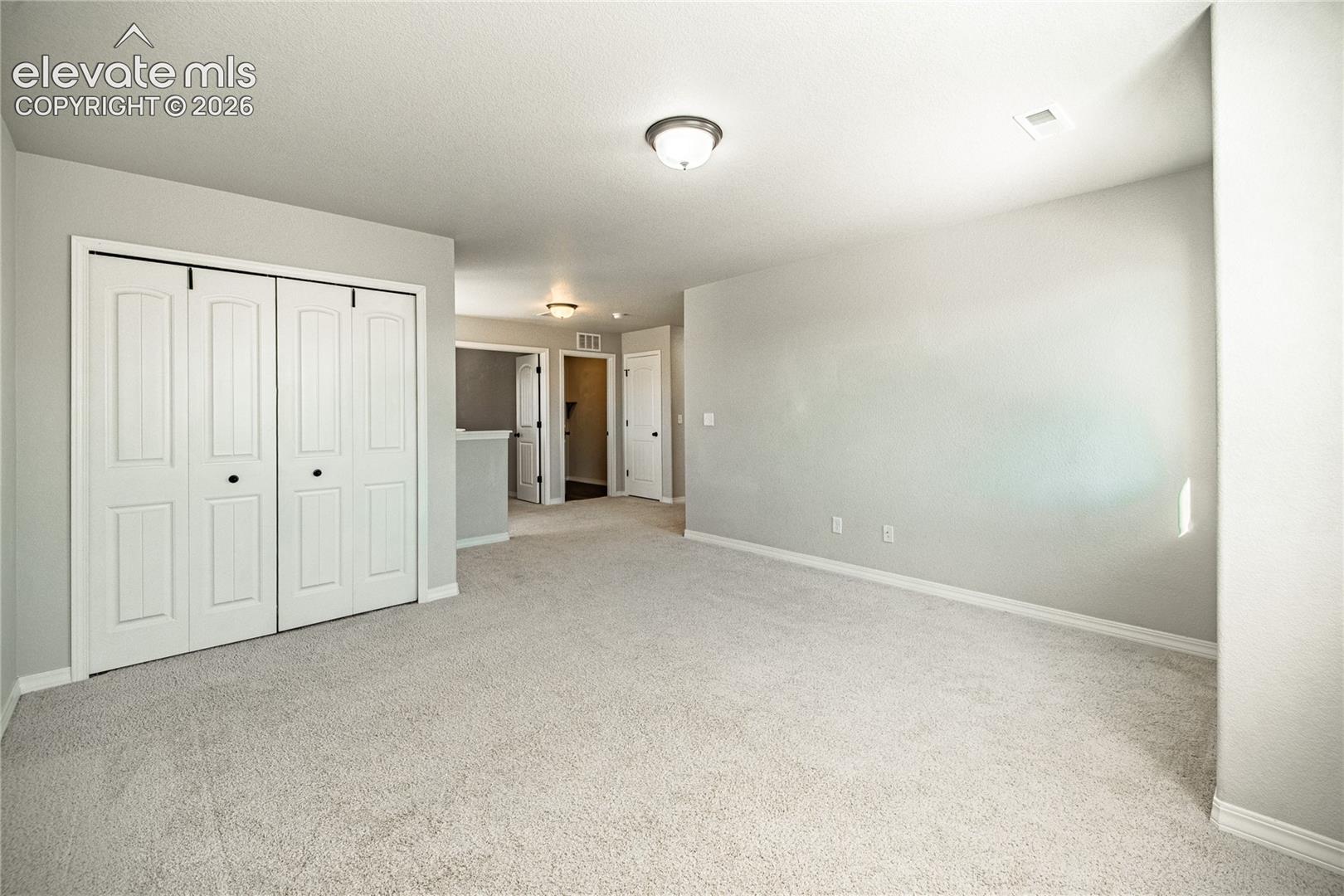 Wall-to-wall carpeting in a neutral tone, bi-fold closet doors, white baseboards, and a flush mount light fixture