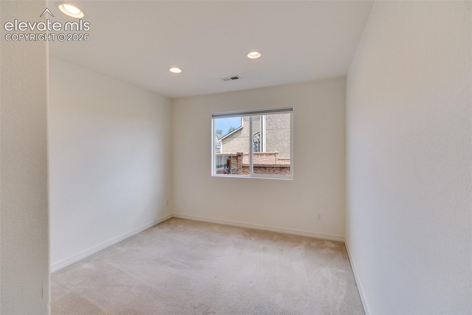 Recessed ceiling lighting illuminates a room with light-toned carpet flooring and a double-pane window