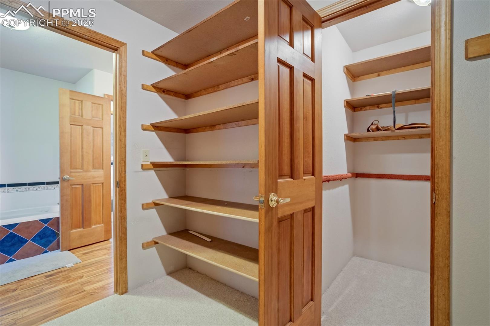 Walk-in closet with extensive built-in shelving, wood-finish doors, carpet flooring, and integrated lighting